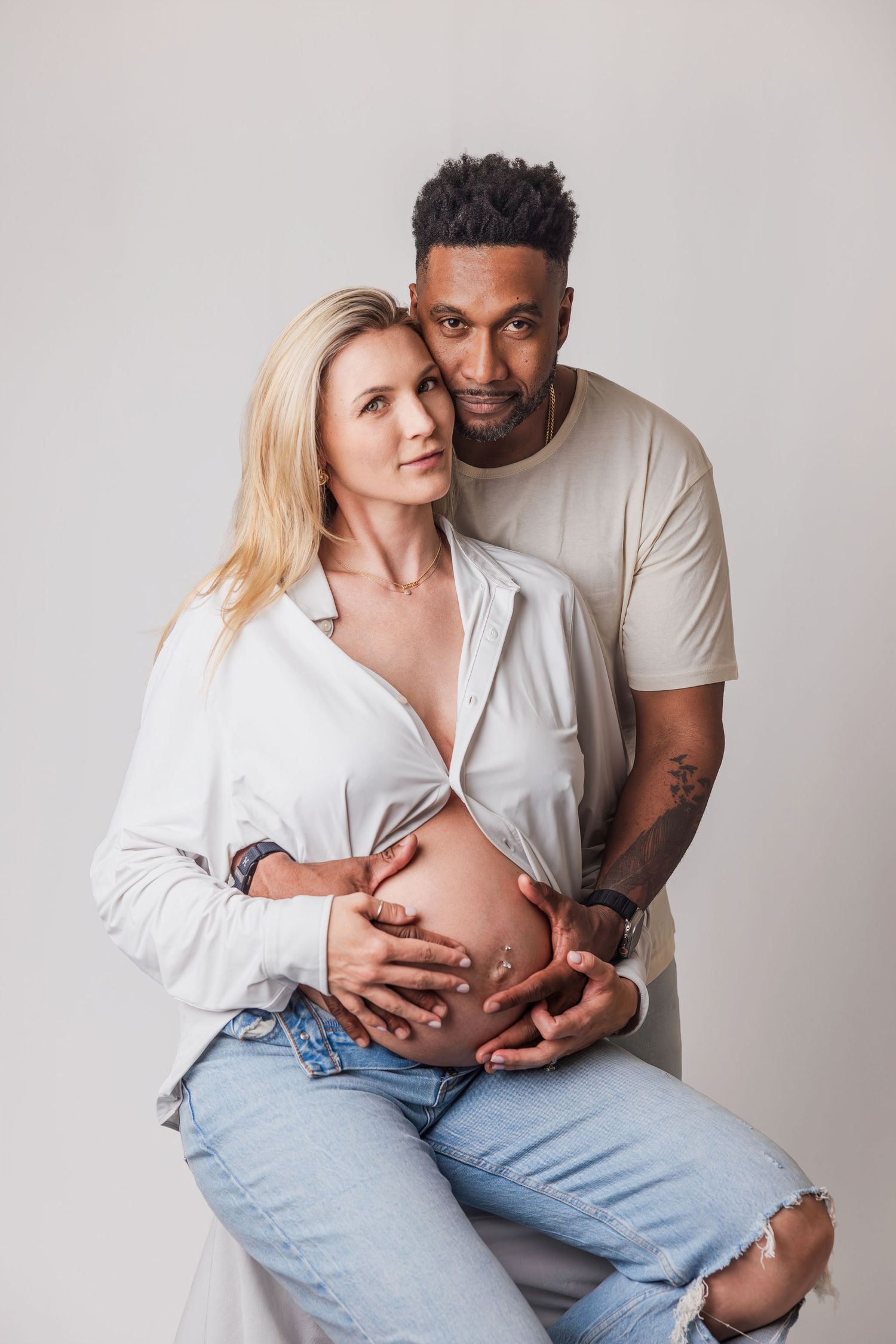 Interracial couple tenderly embrace pregnant belly in professional studio portrait.