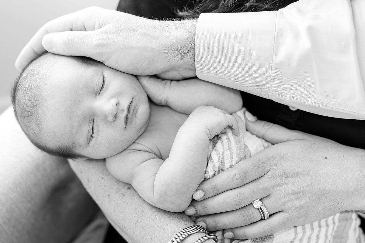 Black and white photo of a sleeping newborn baby cradled in an adults hands.