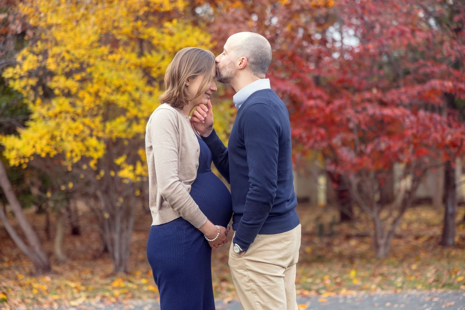 Couple sharing a tender moment during fall maternity photo shoot surrounded by colorful autumn foliage.