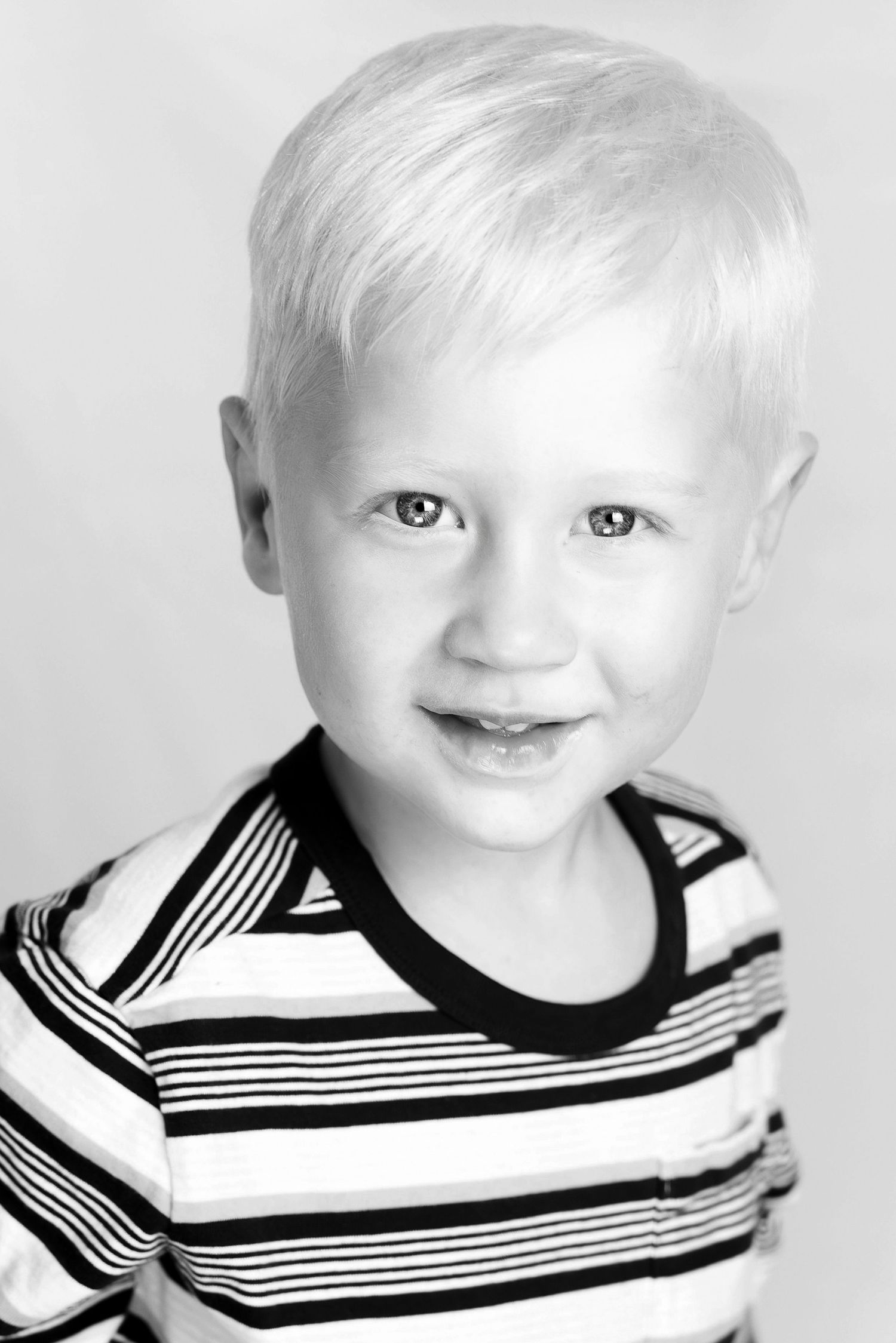 Black and white portrait of a smiling young blonde boy wearing a striped shirt.