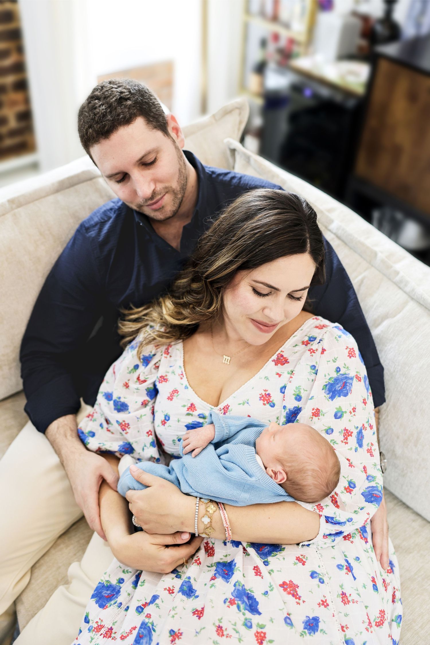 A couple sitting on a couch together, lovingly gazing at their newborn baby wrapped in blue.