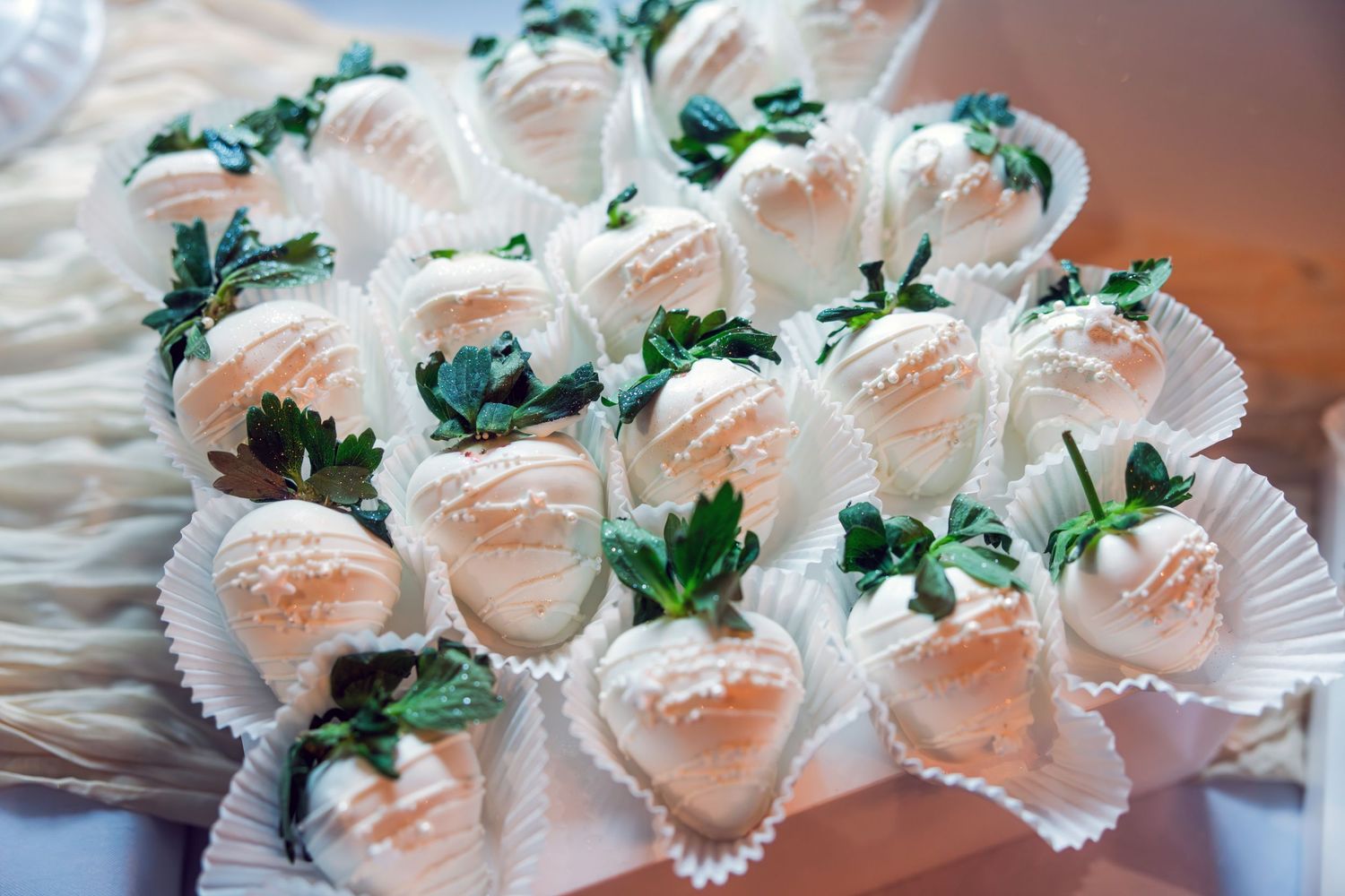 White chocolate-dipped strawberries with decorative drizzle arranged in paper cups on a platter.