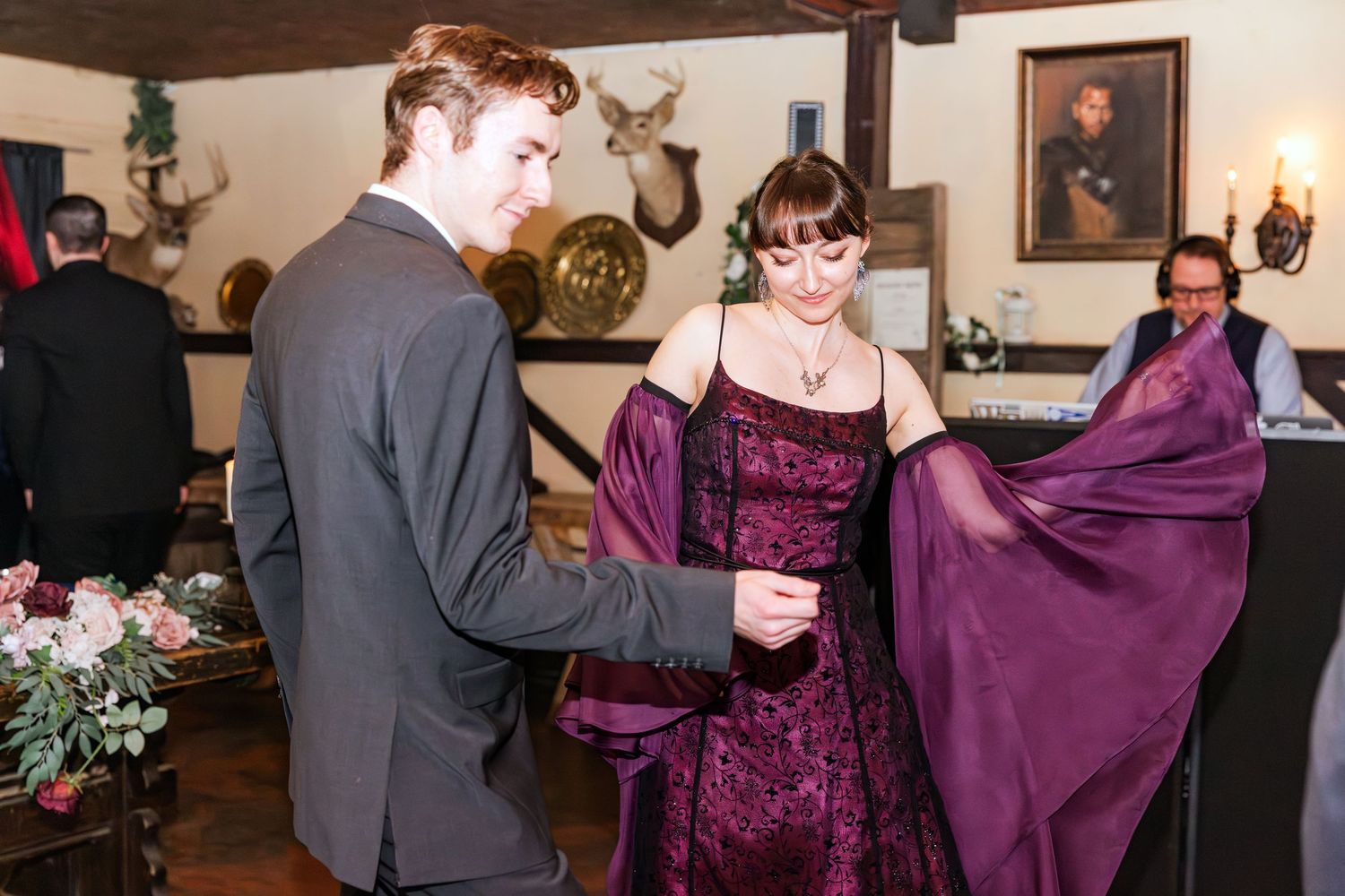 Young couple at formal event, man helping woman in purple gown with her wrap.