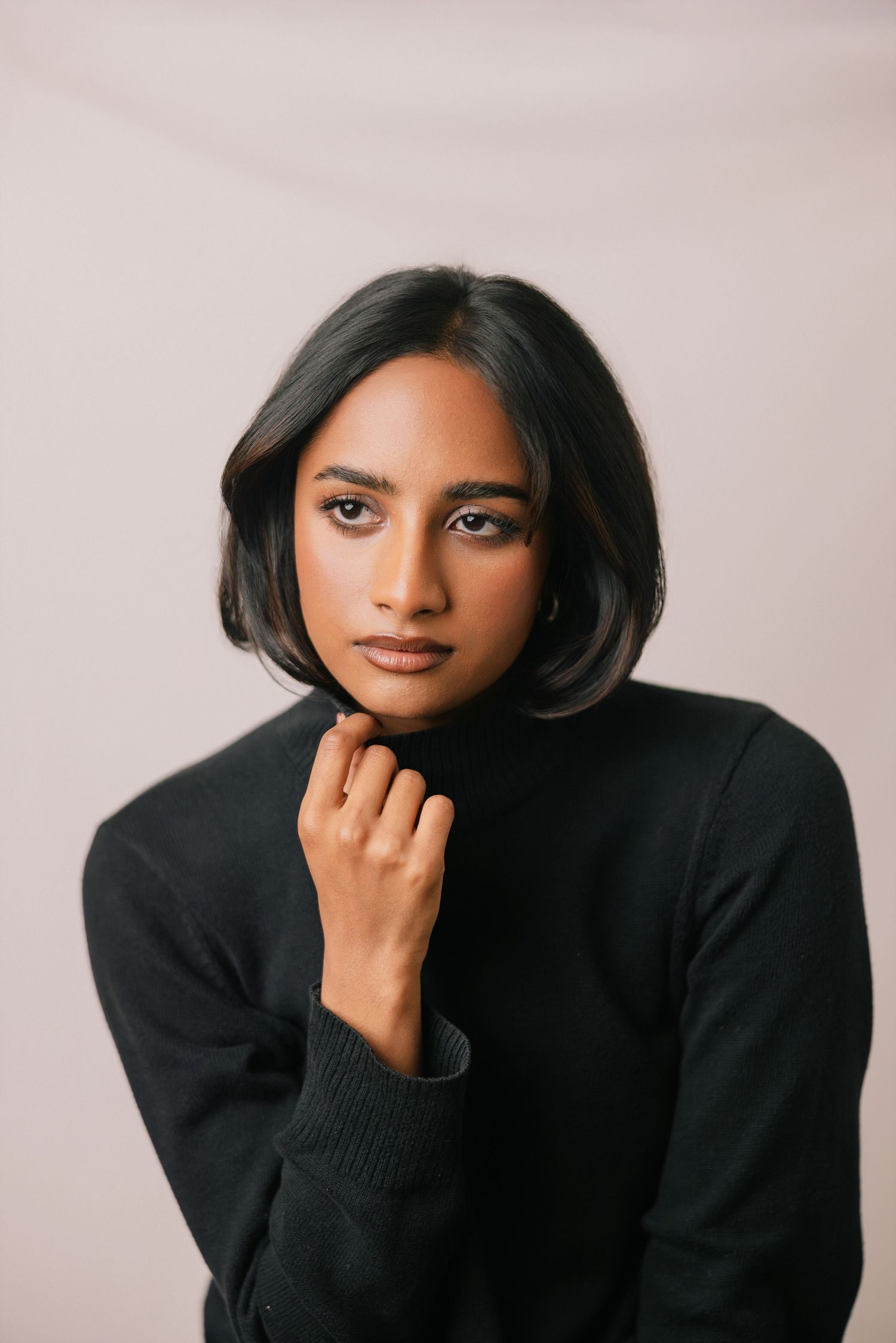 Young woman in black turtleneck sweater with bob haircut posing against neutral background.