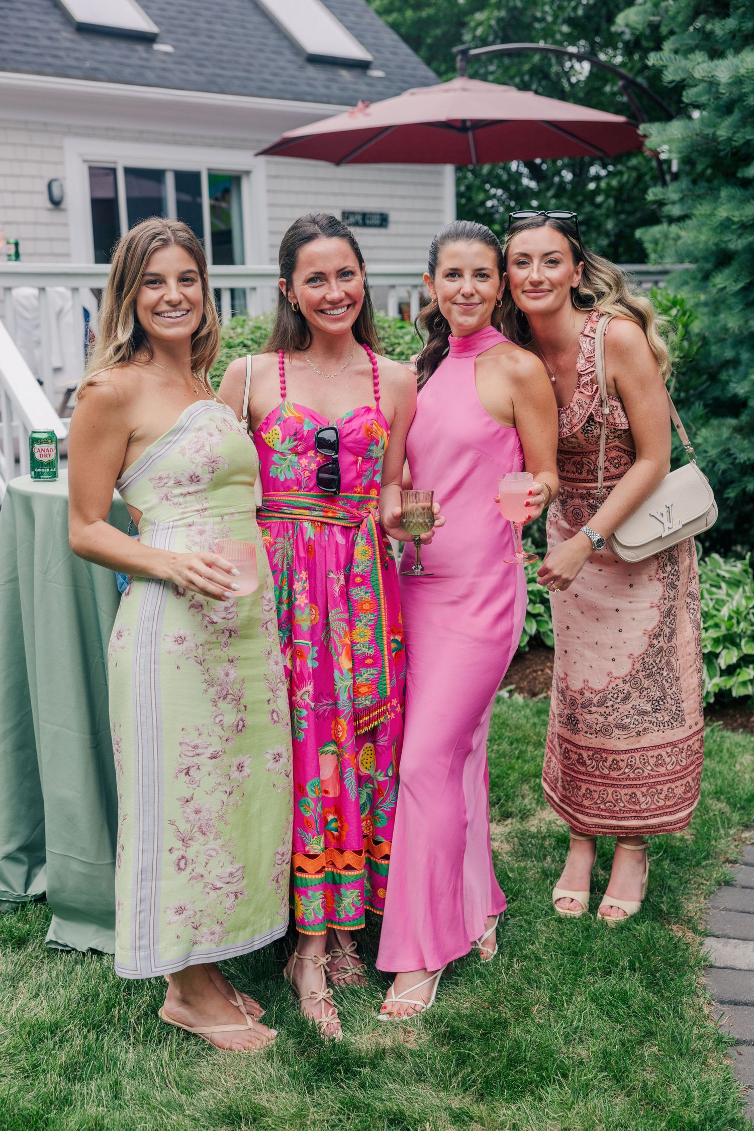 Four smiling women in vibrant summer dresses posing together at an outdoor garden wedding party.