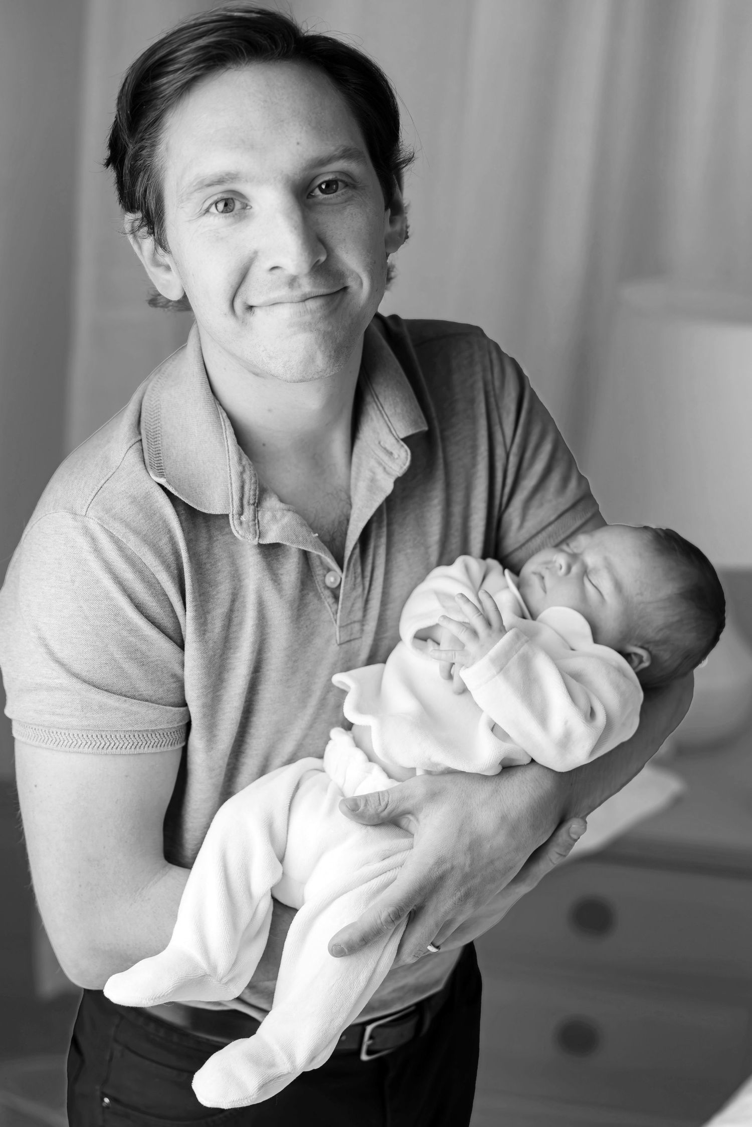 Black and white portrait of a smiling young man holding a newborn baby.