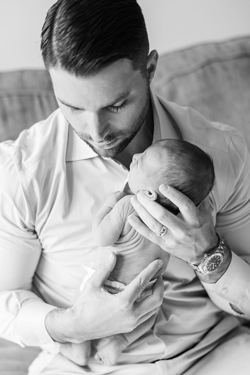 Black and white photo of a loving father cradling his newborn baby, wearing a dress shirt and watch.