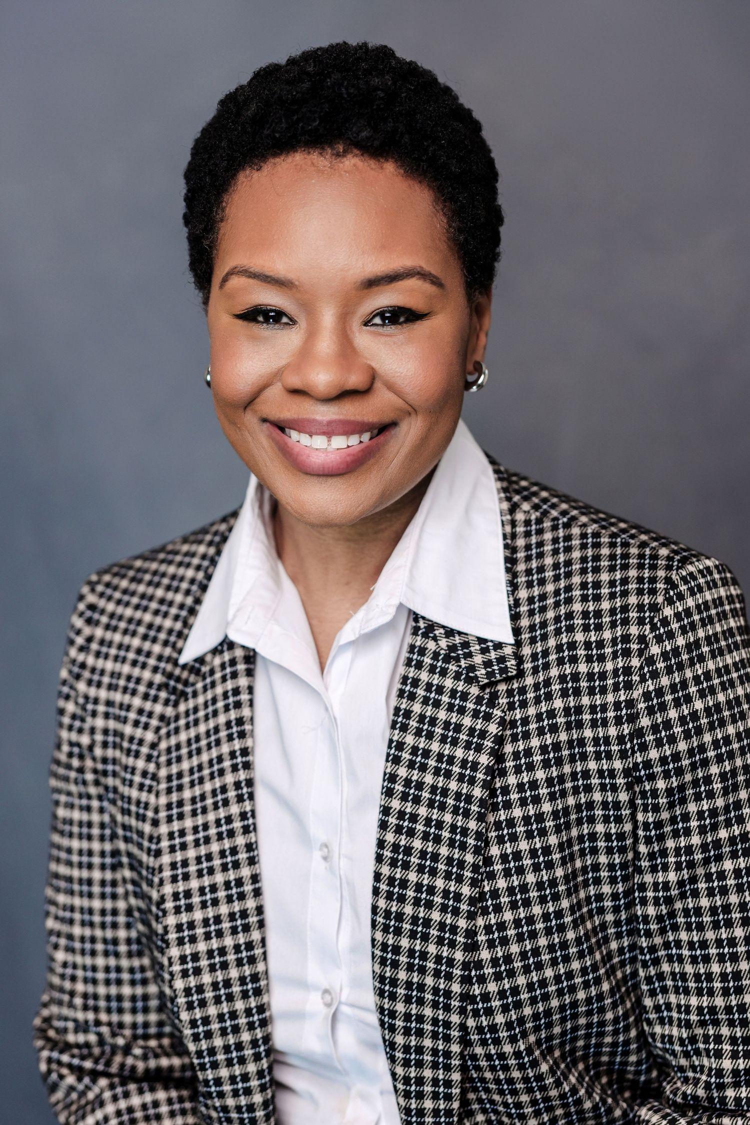 Professional woman in houndstooth blazer and white shirt smiling against gray background.