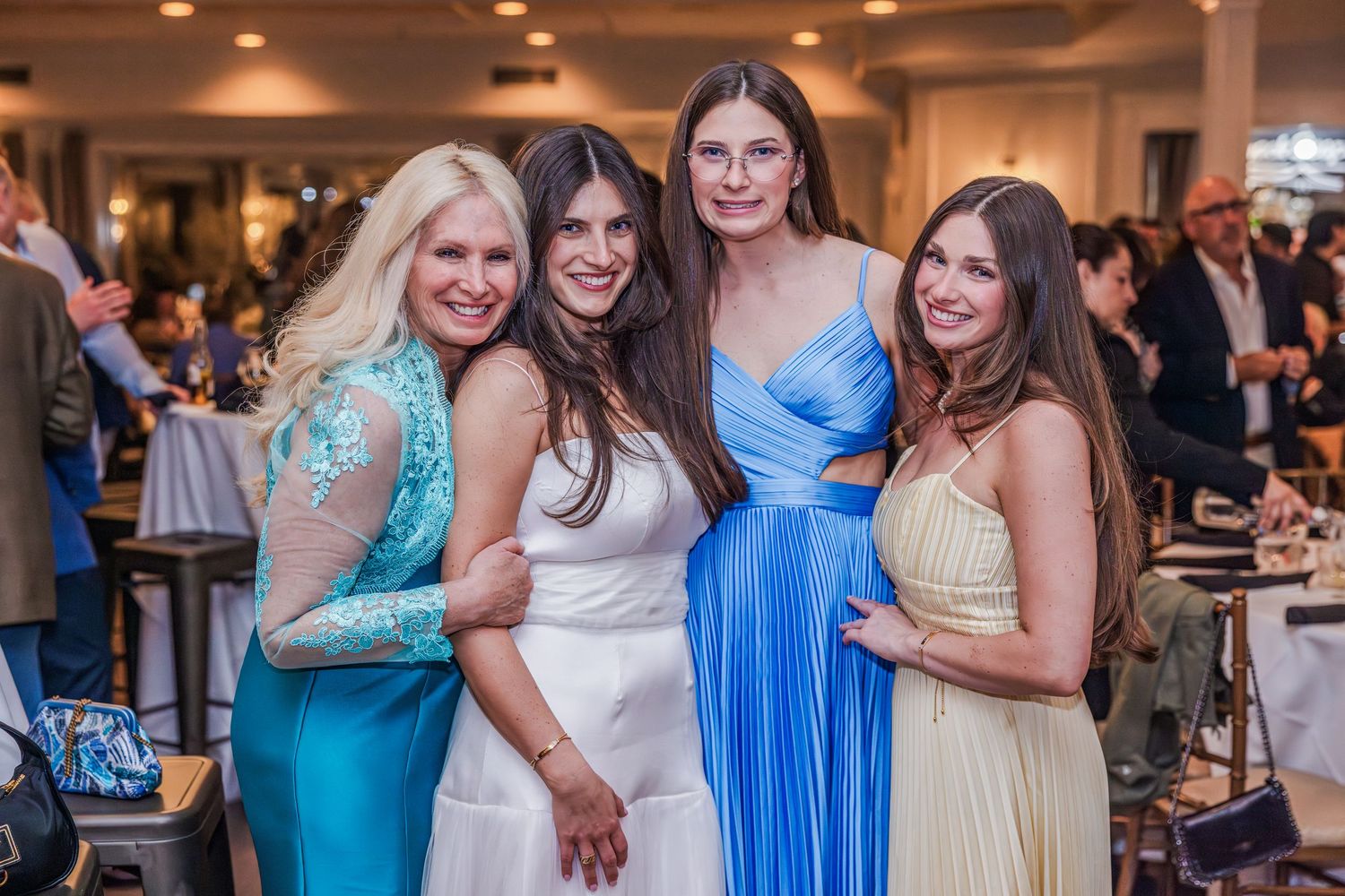 Four women in blue and white formal gowns posing together at an elegant party.
