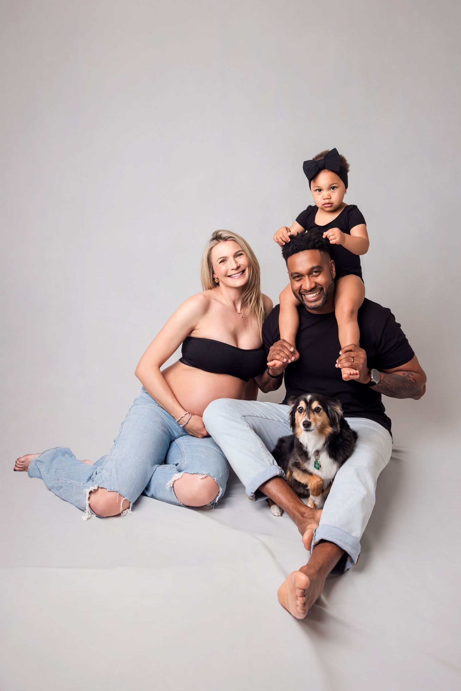 Happy interracial family with pregnant mom, dad, toddler, and dog in studio.