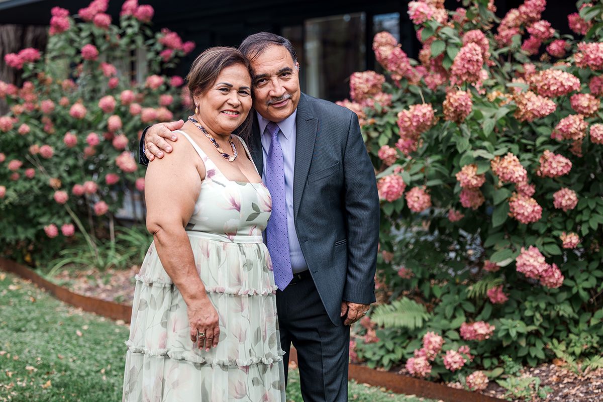 Smiling couple embracing outdoors in front of blooming pink hydrangea bushes in a garden.