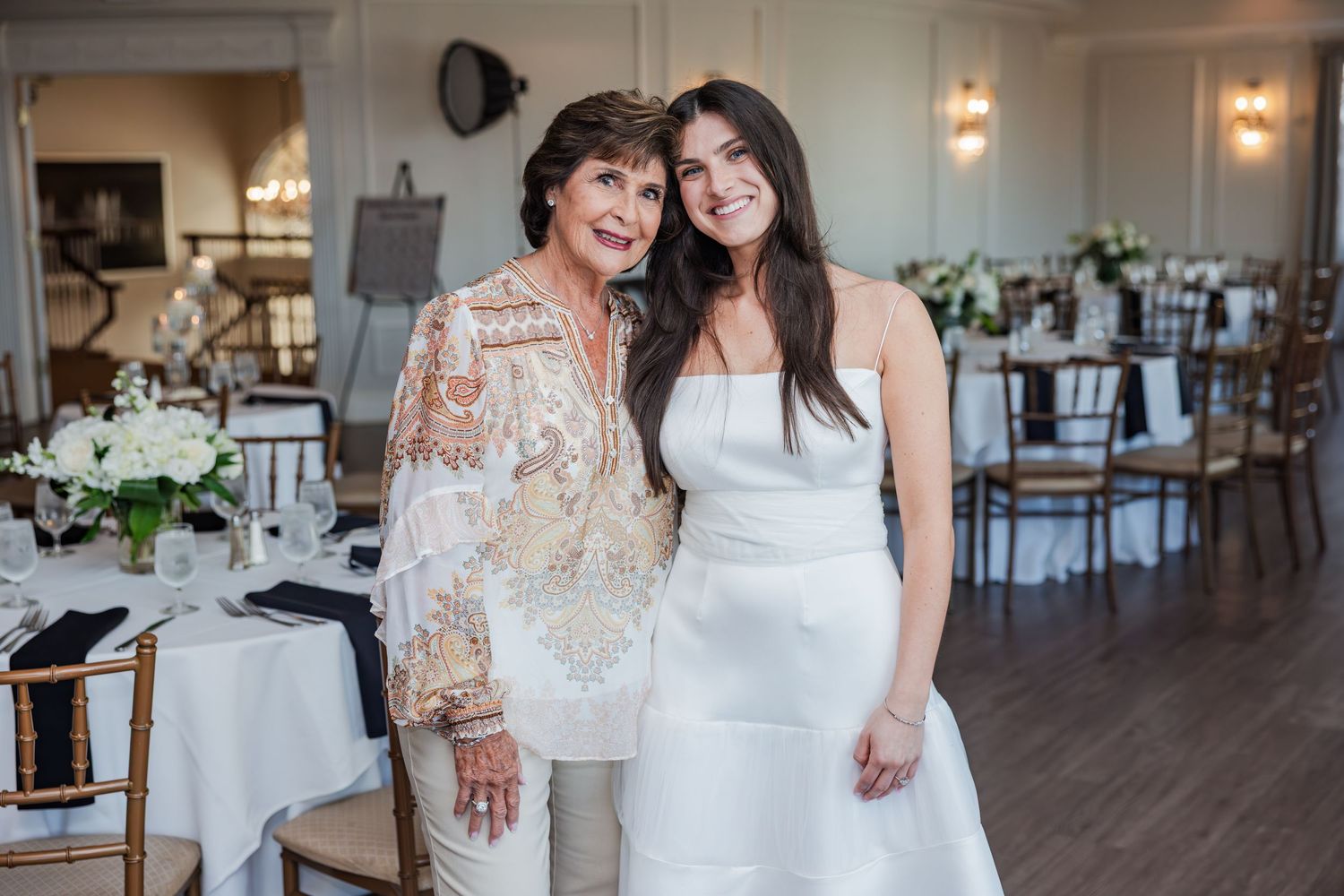 Two women posing together in a beautifully decorated wedding reception venue setting.