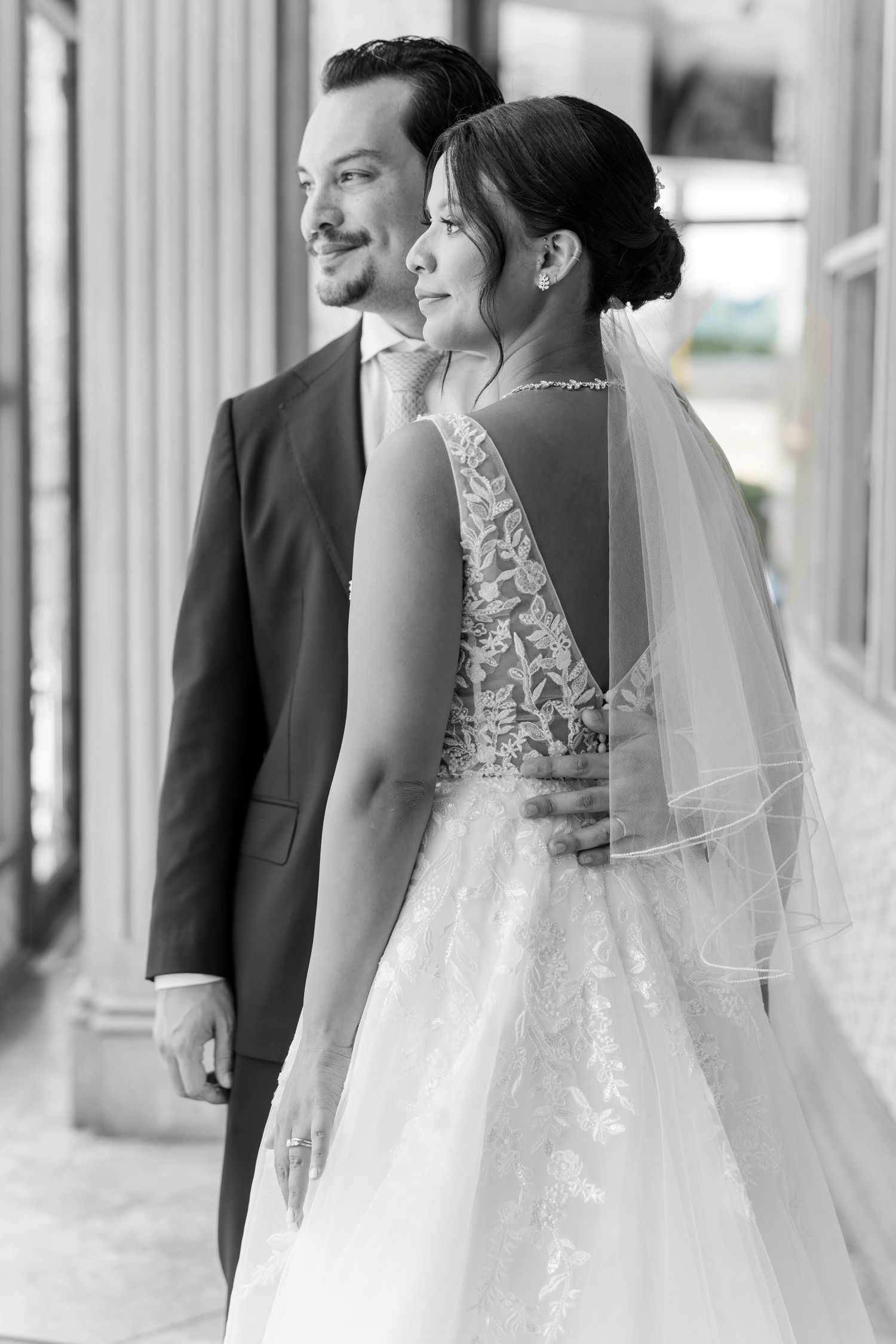 Black and white portrait of bride and groom in formal wedding attire standing by ornate columns.