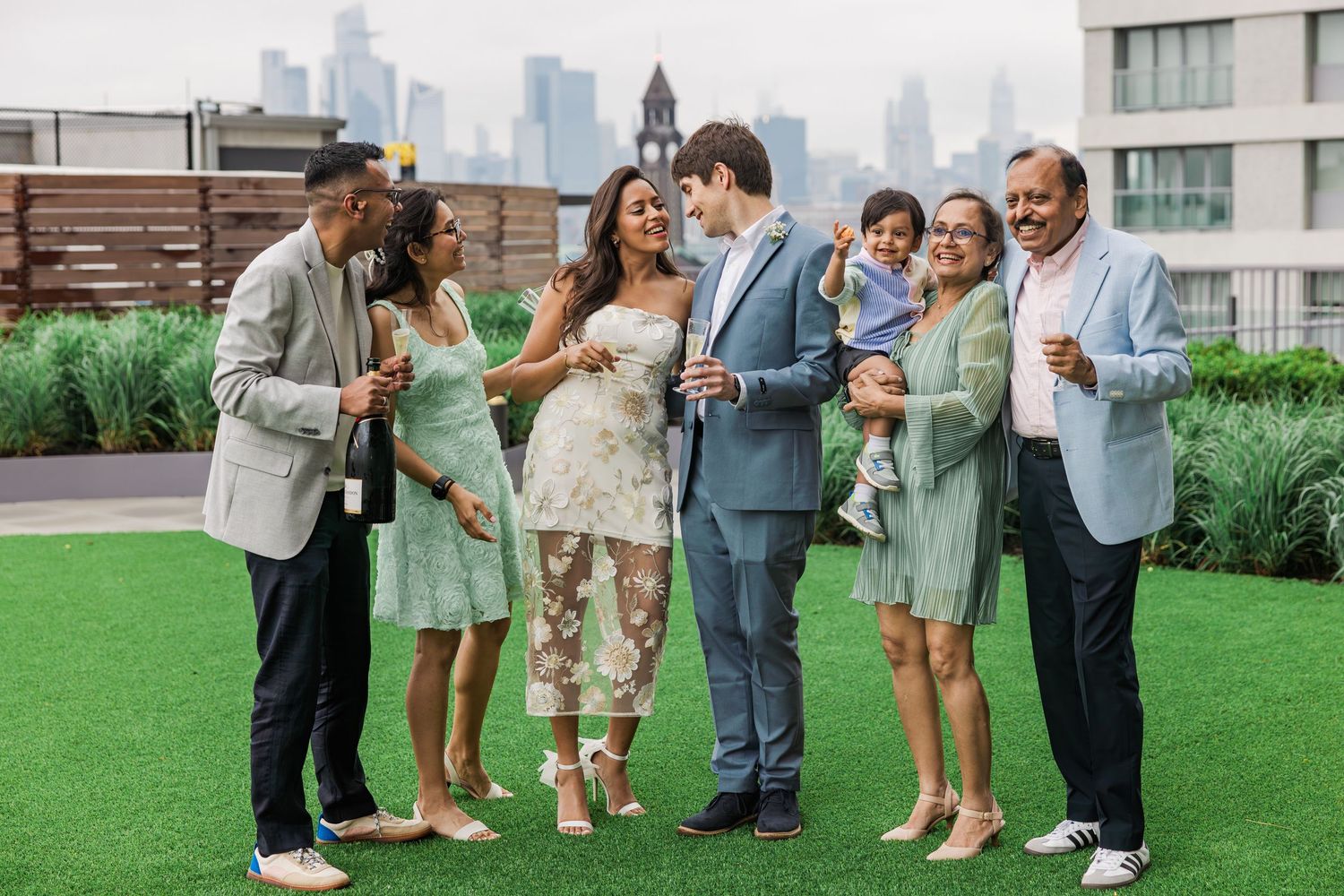Joyful wedding party celebrating on rooftop terrace with New York City skyline in the background.