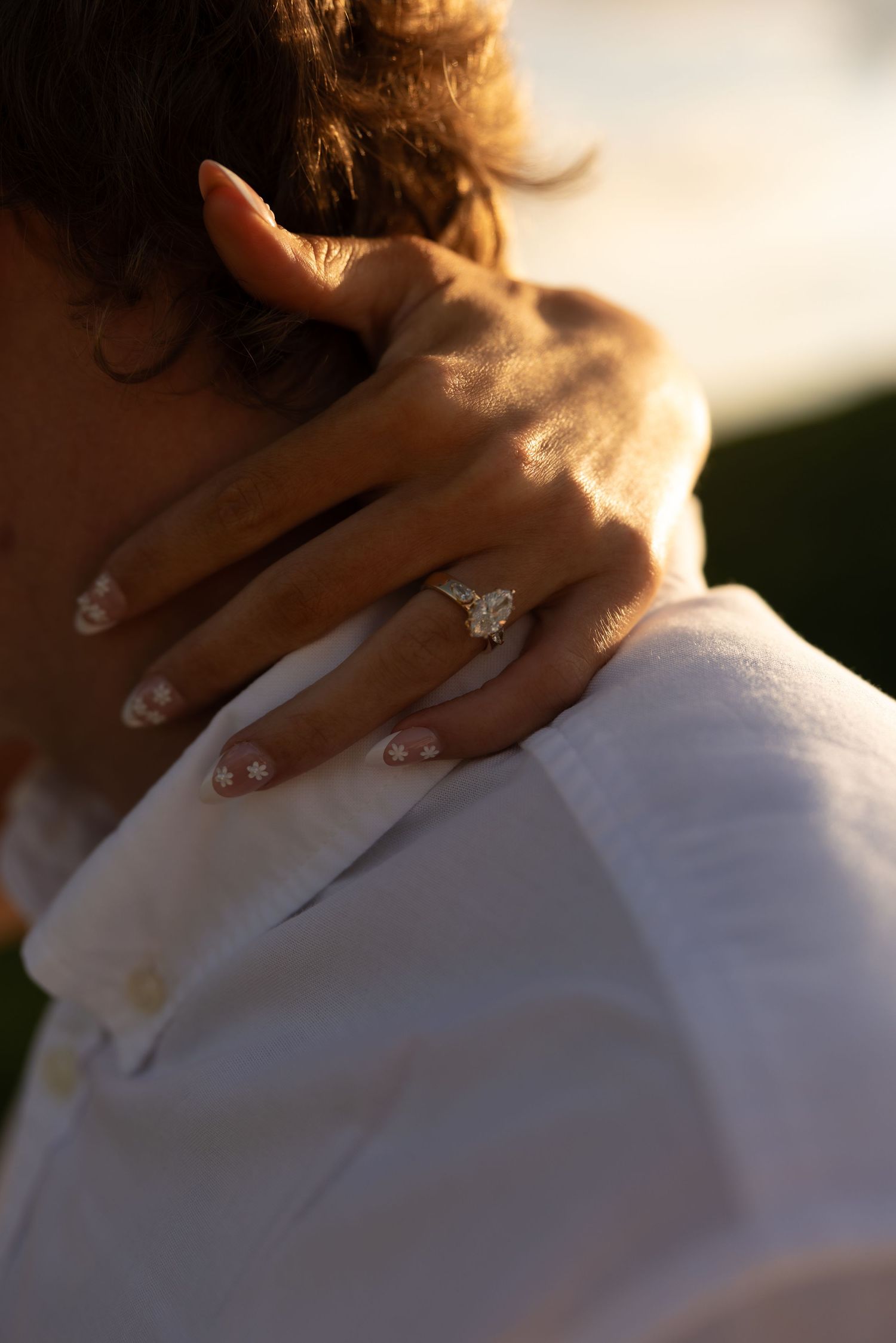 Close-up of womans hand with diamond engagement ring resting on mans white shirt collar.