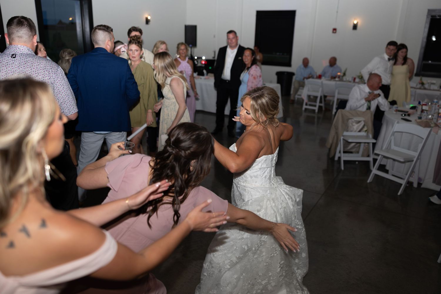 Bride in lace wedding dress dancing energetically with guests at fun wedding reception.