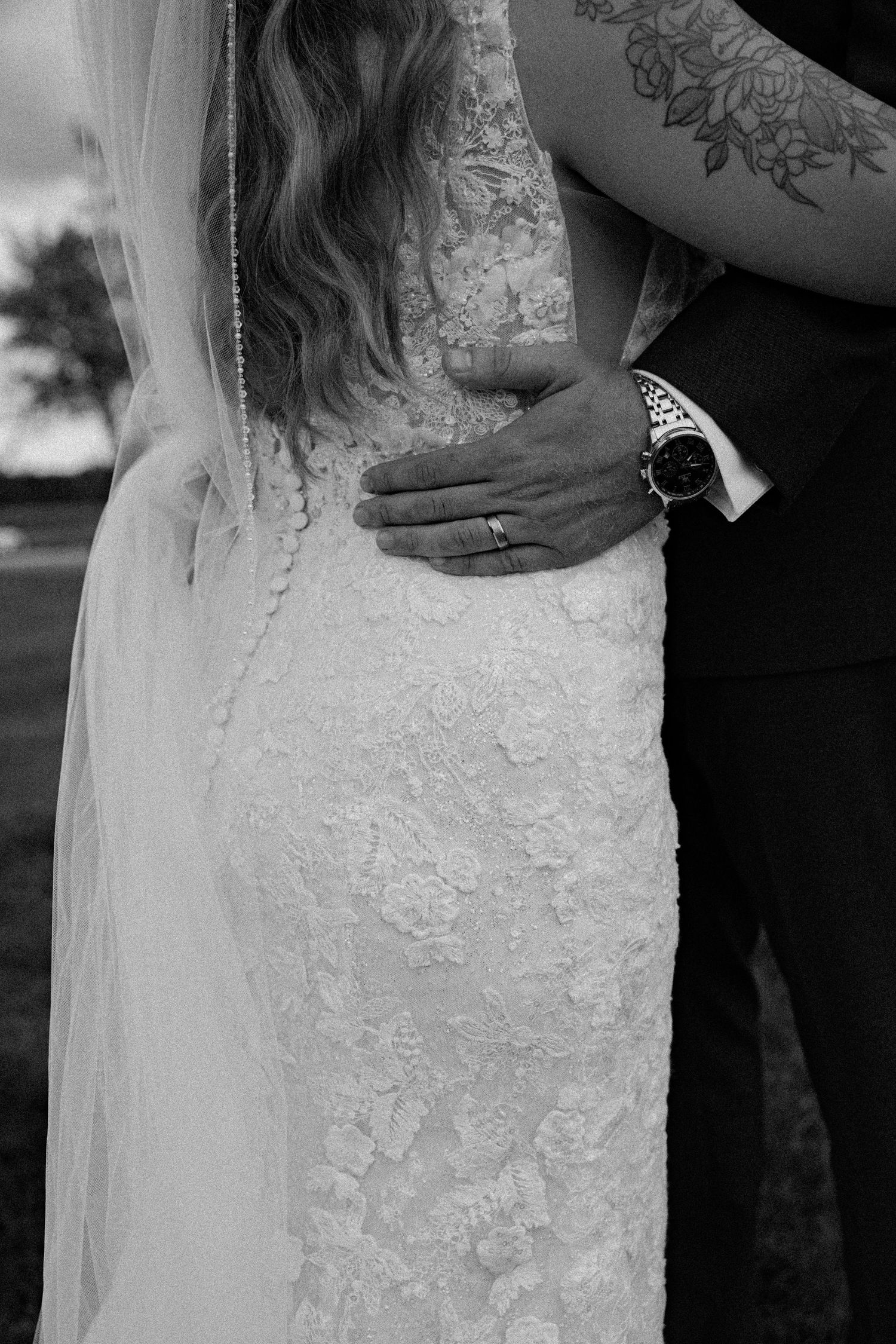 Black and white close-up of groom embracing bride in lace wedding gown with wedding ring detail.