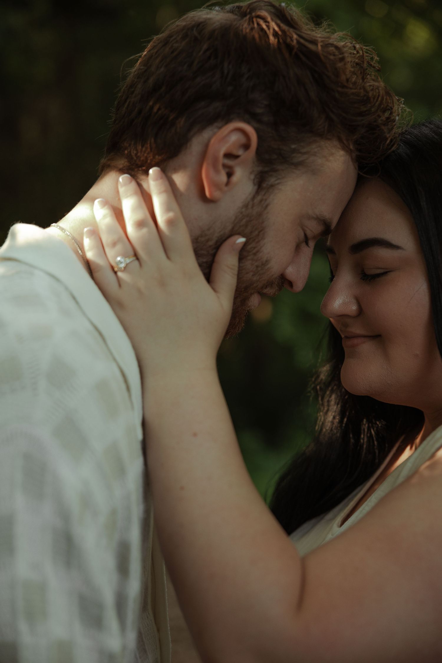 Intimate close-up of couple touching foreheads tenderly, woman with engagement ring cradling man's face softly.