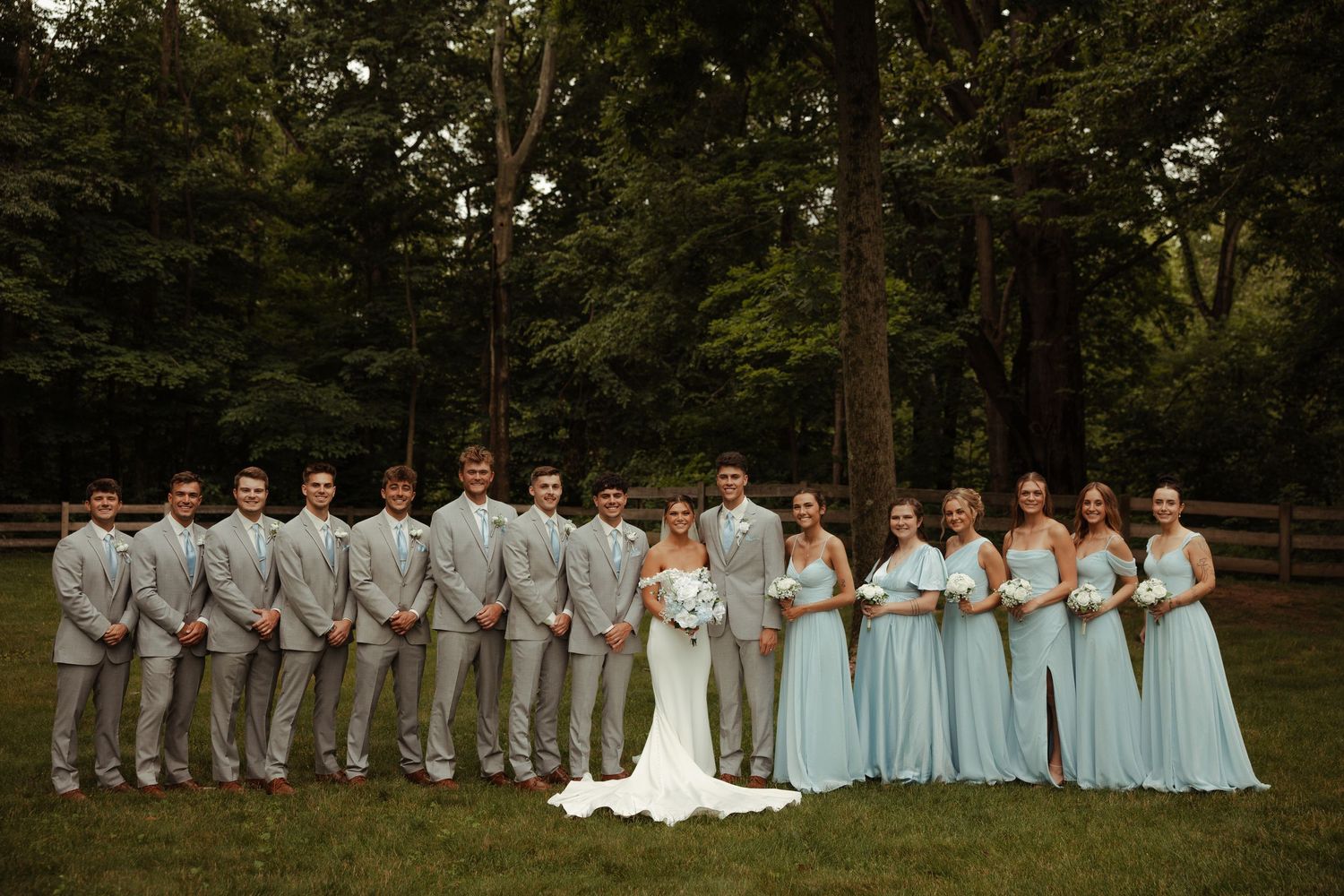 Wedding party lines up outdoors with bridesmaids in mint blue dresses and groomsmen in gray suits flanking bride and groom.