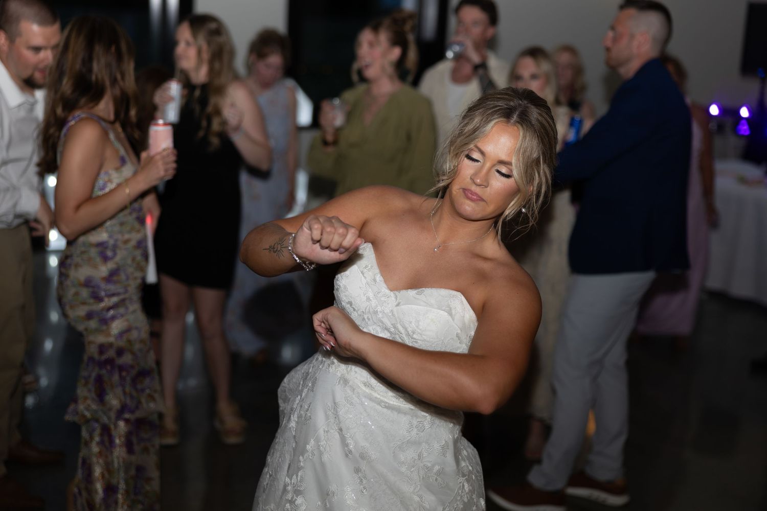Bride in strapless lace wedding gown dancing joyfully surrounded by guests at reception.