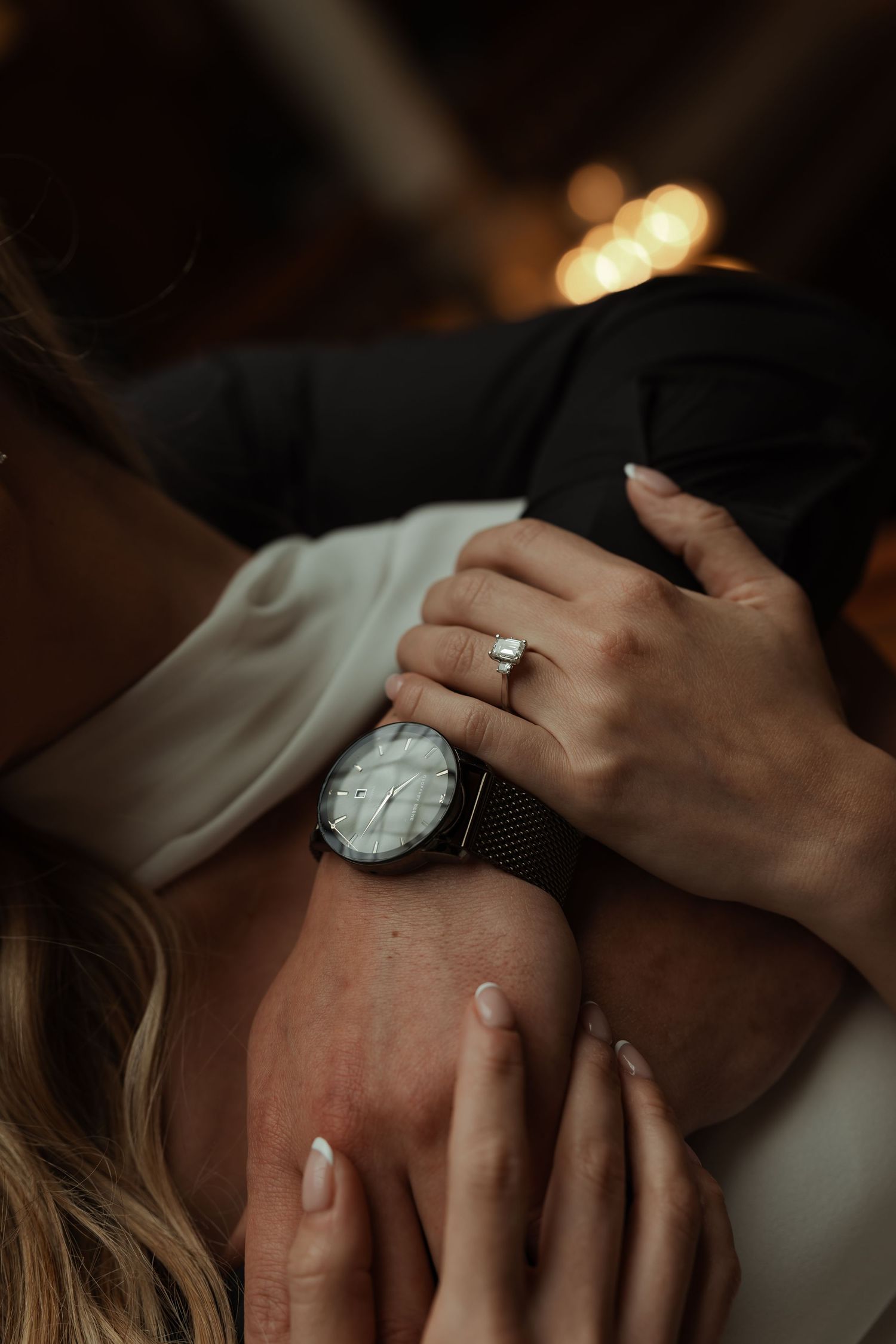 Close-up of couple embracing, bride wearing diamond engagement ring and groom wearing elegant watch.