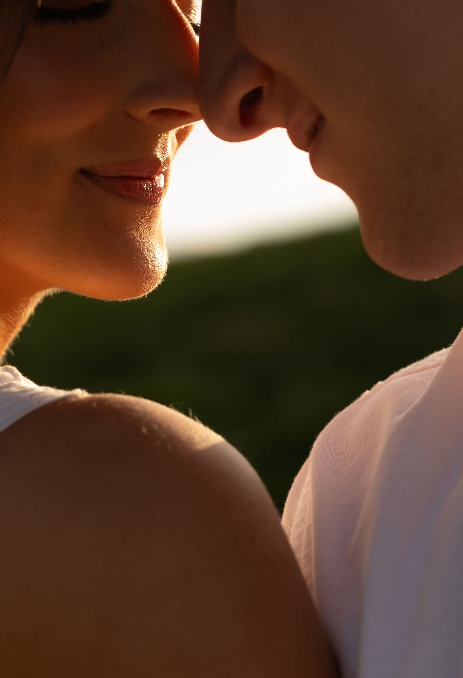Romantic close-up of couple almost kissing in warm golden sunlight outdoors.