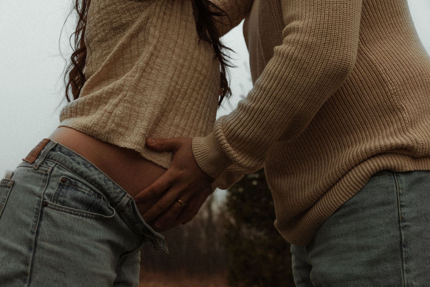 Close-up of partner gently holding pregnant womans baby bump during outdoor maternity shoot.