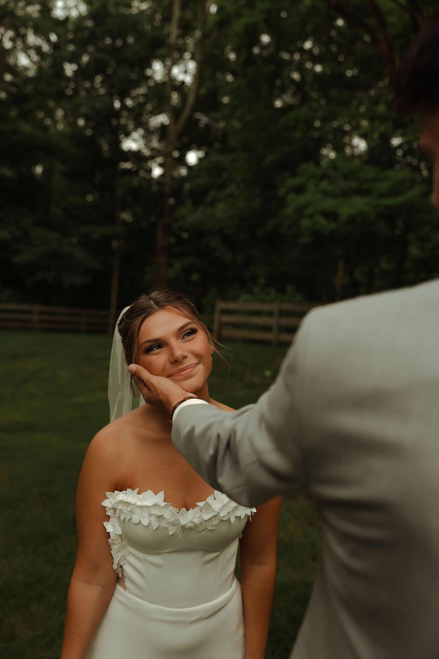 Groom gently cups brides face as she smiles lovingly in outdoor wedding portrait.