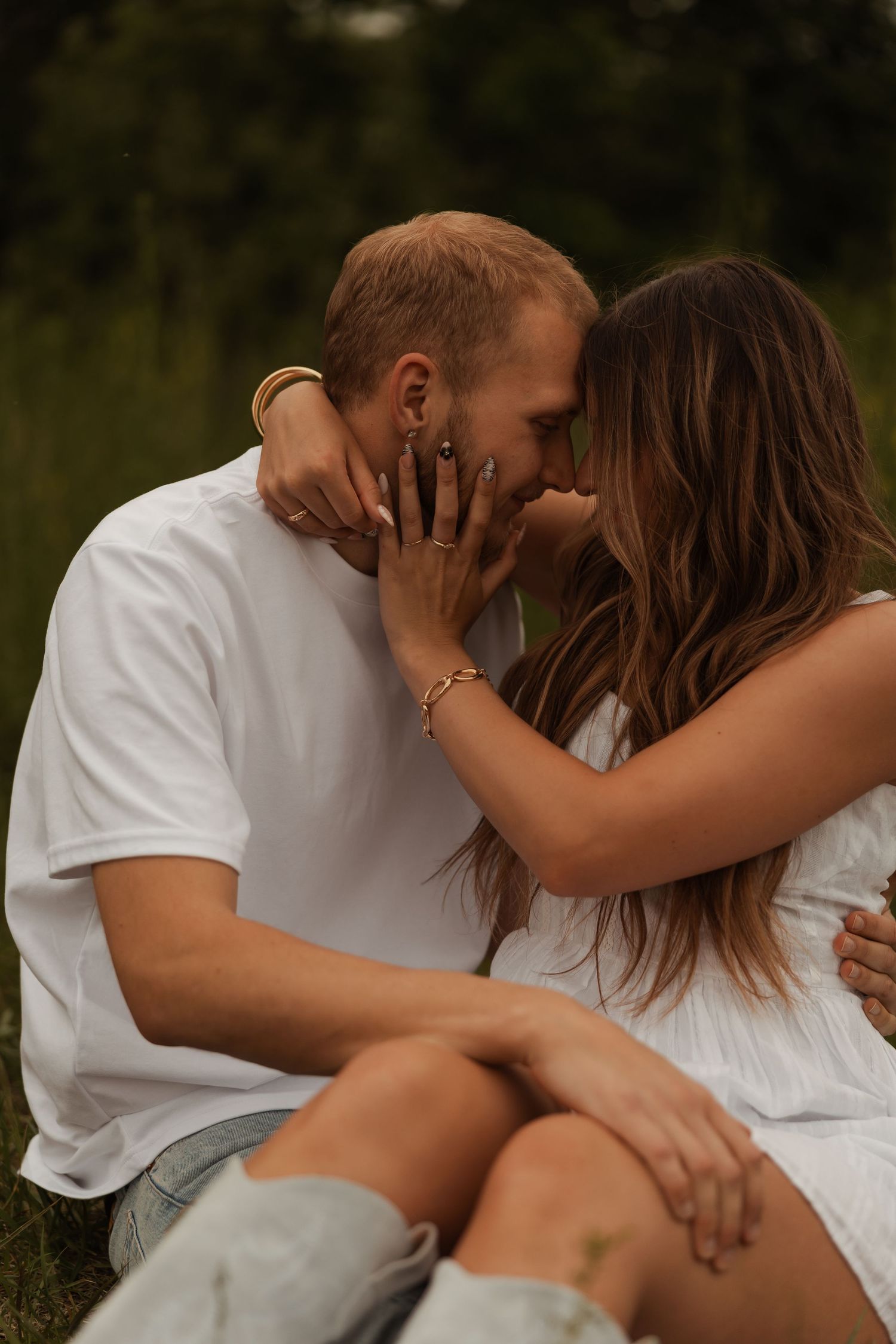 A couple shares a kiss outdoors in a grassy field, the woman wearing white cowboy boots and a dress.