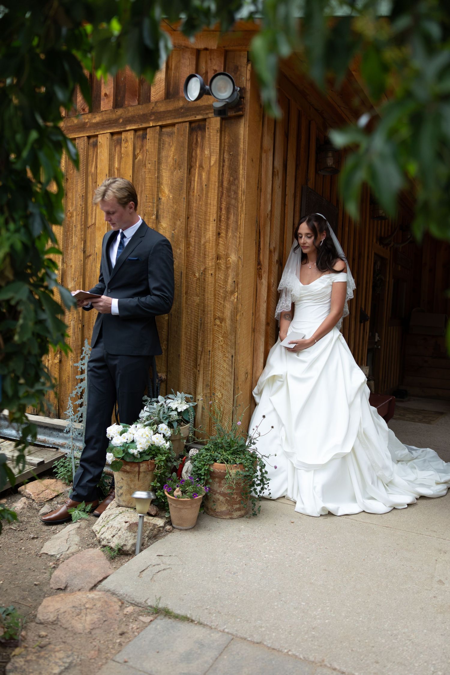 Bride in white gown and groom in dark suit share private vows outside rustic wooden barn wedding venue.