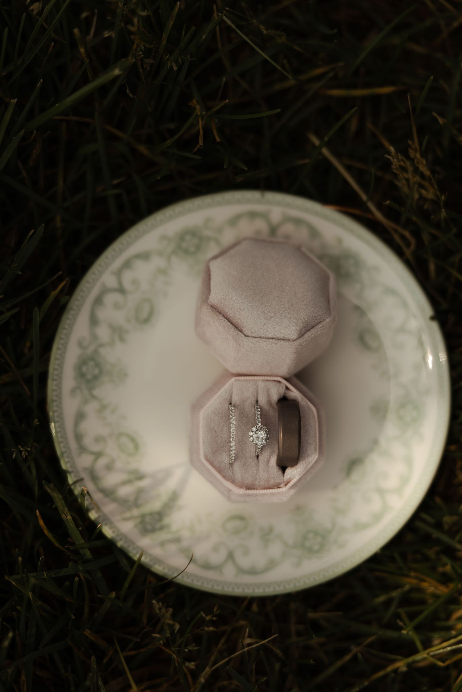 Diamond engagement and wedding rings displayed in pink velvet octagonal ring box on decorative plate.