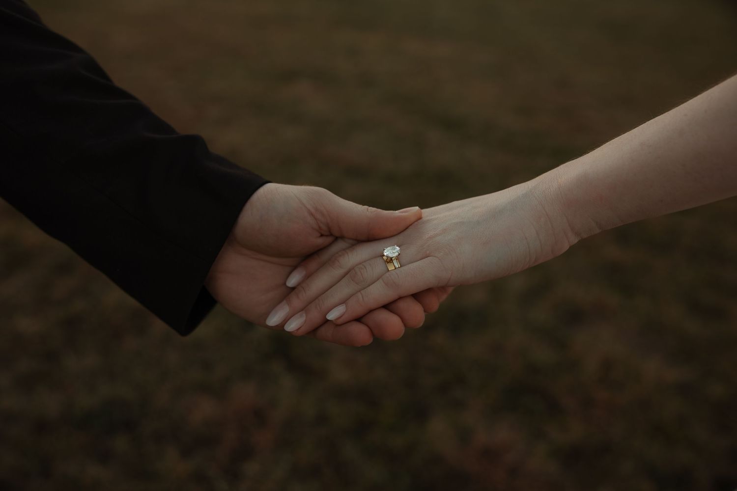 Close-up of bride and groom holding hands, showcasing a delicate diamond engagement ring.