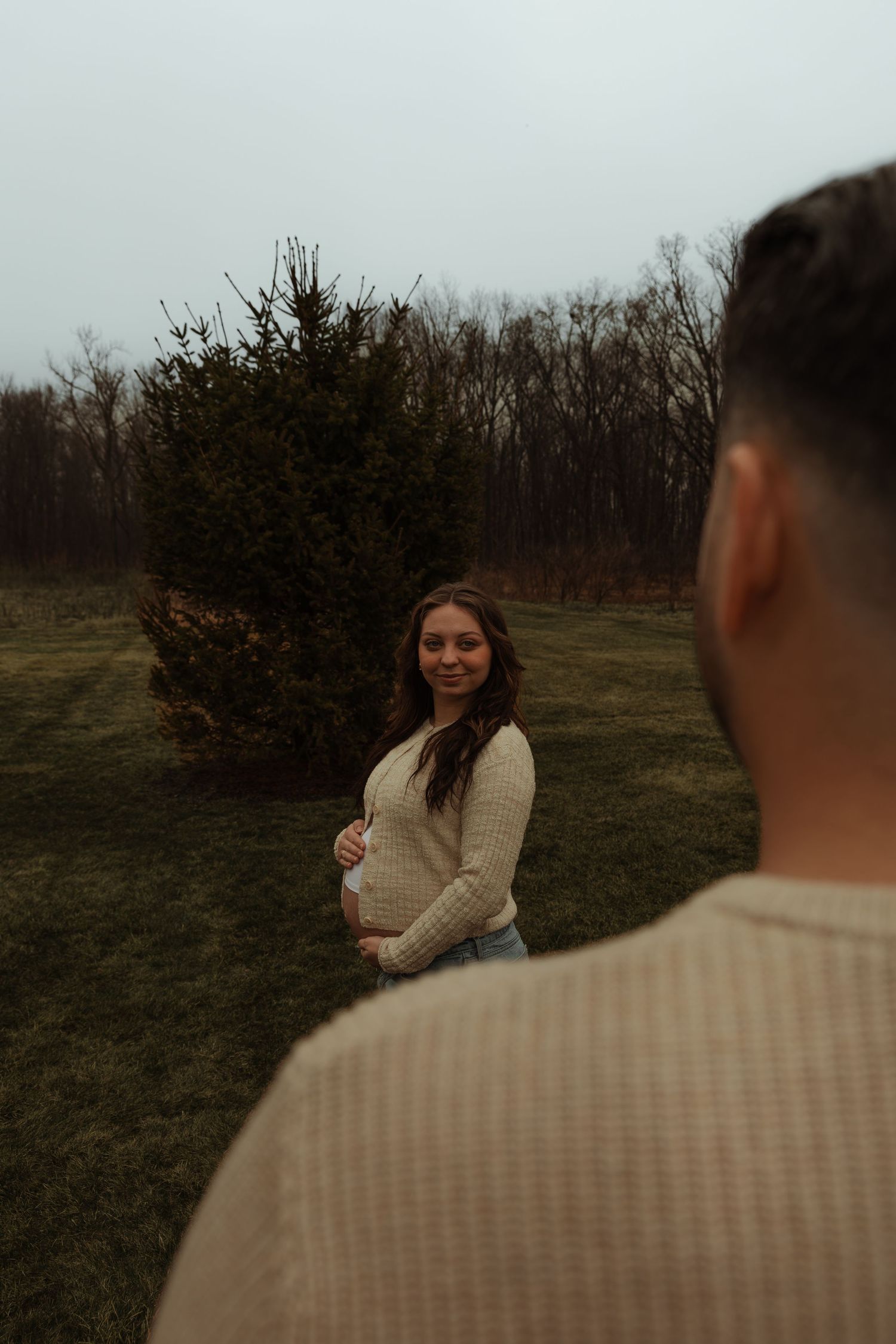 Pregnant woman cradling baby bump smiling at partner during outdoor maternity photoshoot.