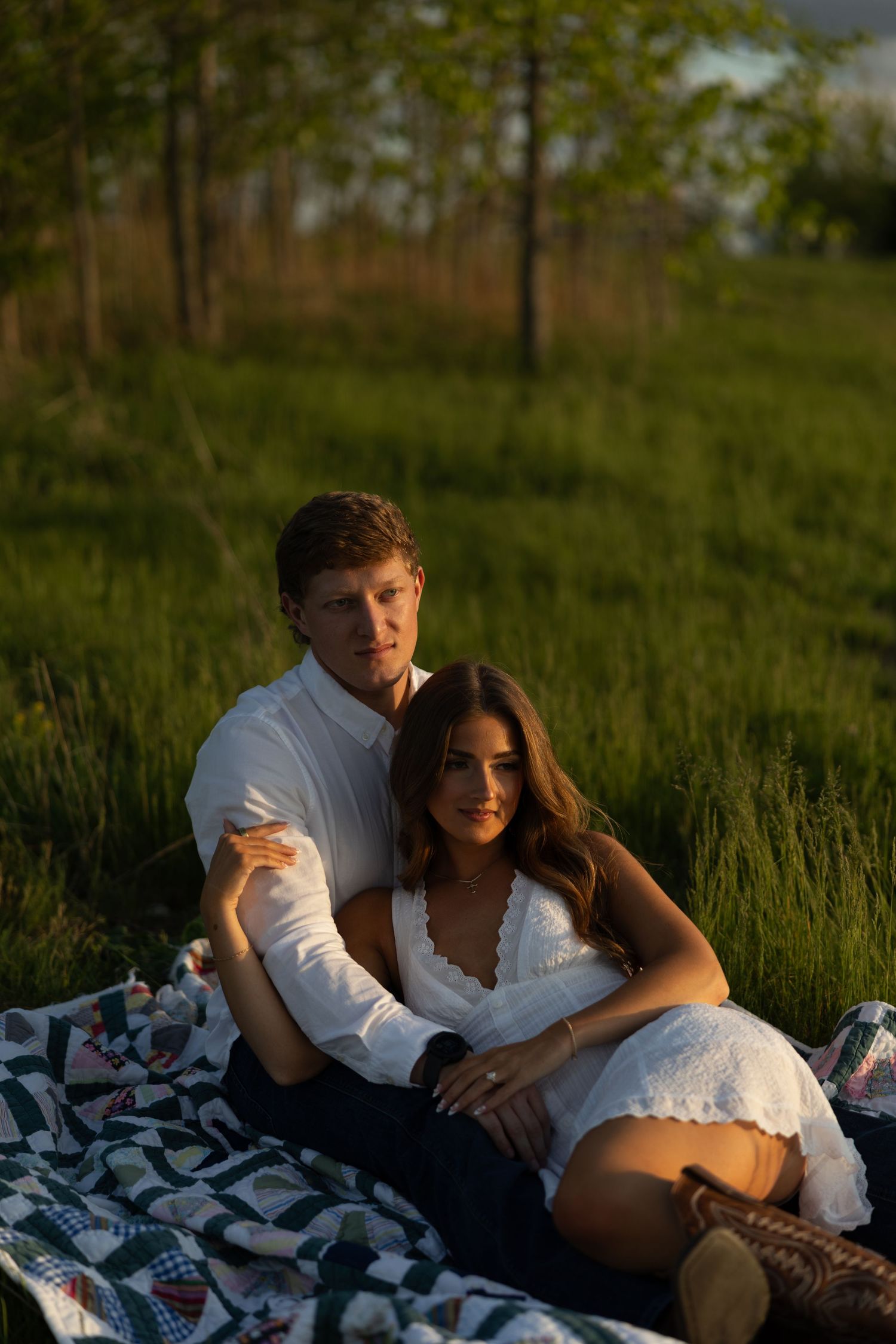 Couple sitting together on a quilt blanket in a sunlit green meadow during golden hour.