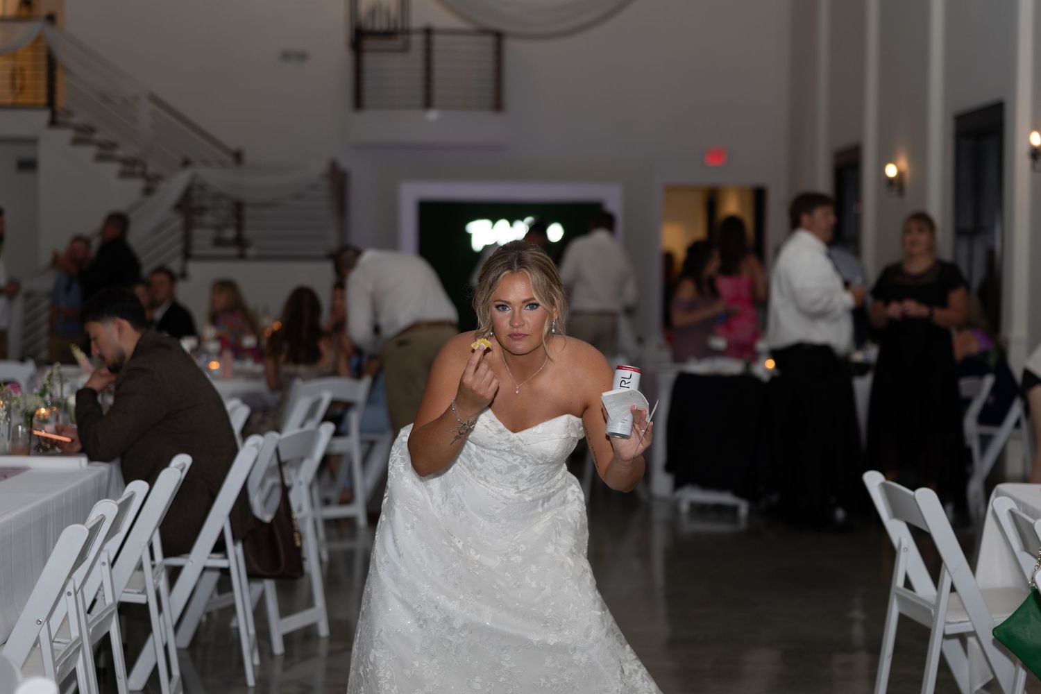 Bride in strapless white wedding gown walking through decorated reception hall with guests.