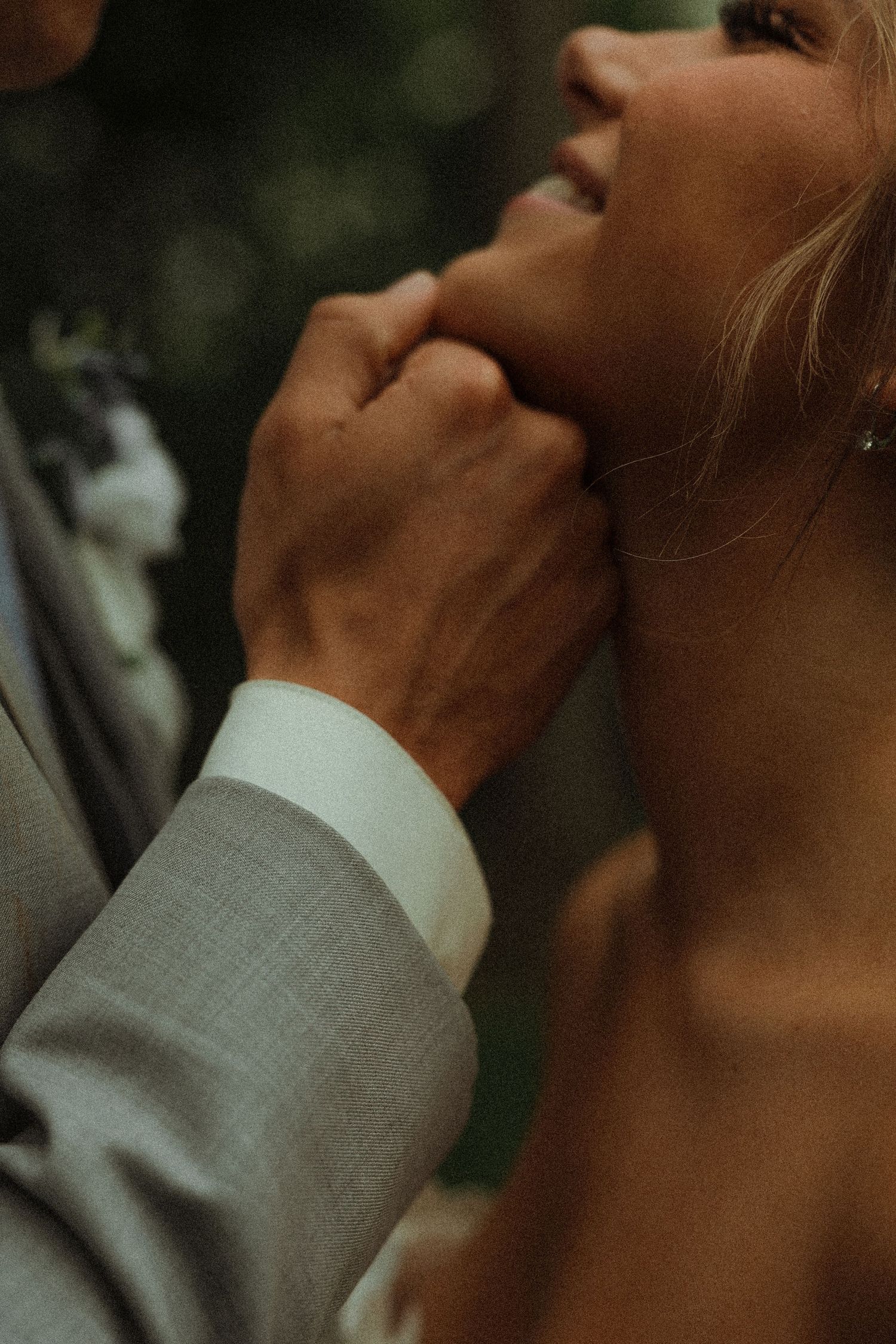 Groom in gray suit gently holds brides chin in tender close-up wedding portrait detail shot.