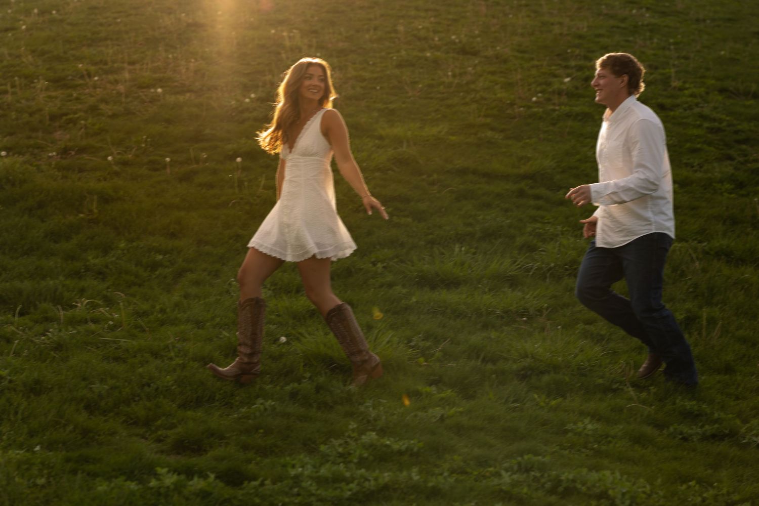 Couple running and playing together in a sunlit green meadow at golden hour.