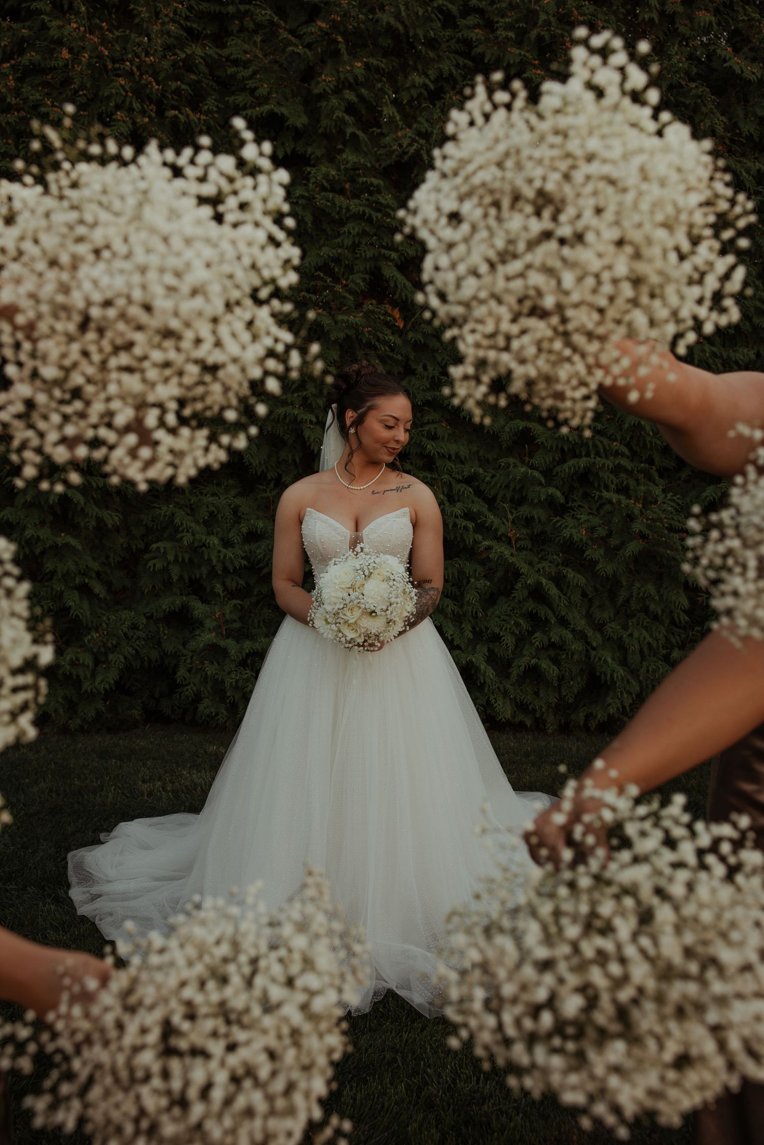 Bride in a white ballgown holds a bouquet surrounded by bridesmaids with baby's breath bouquets.