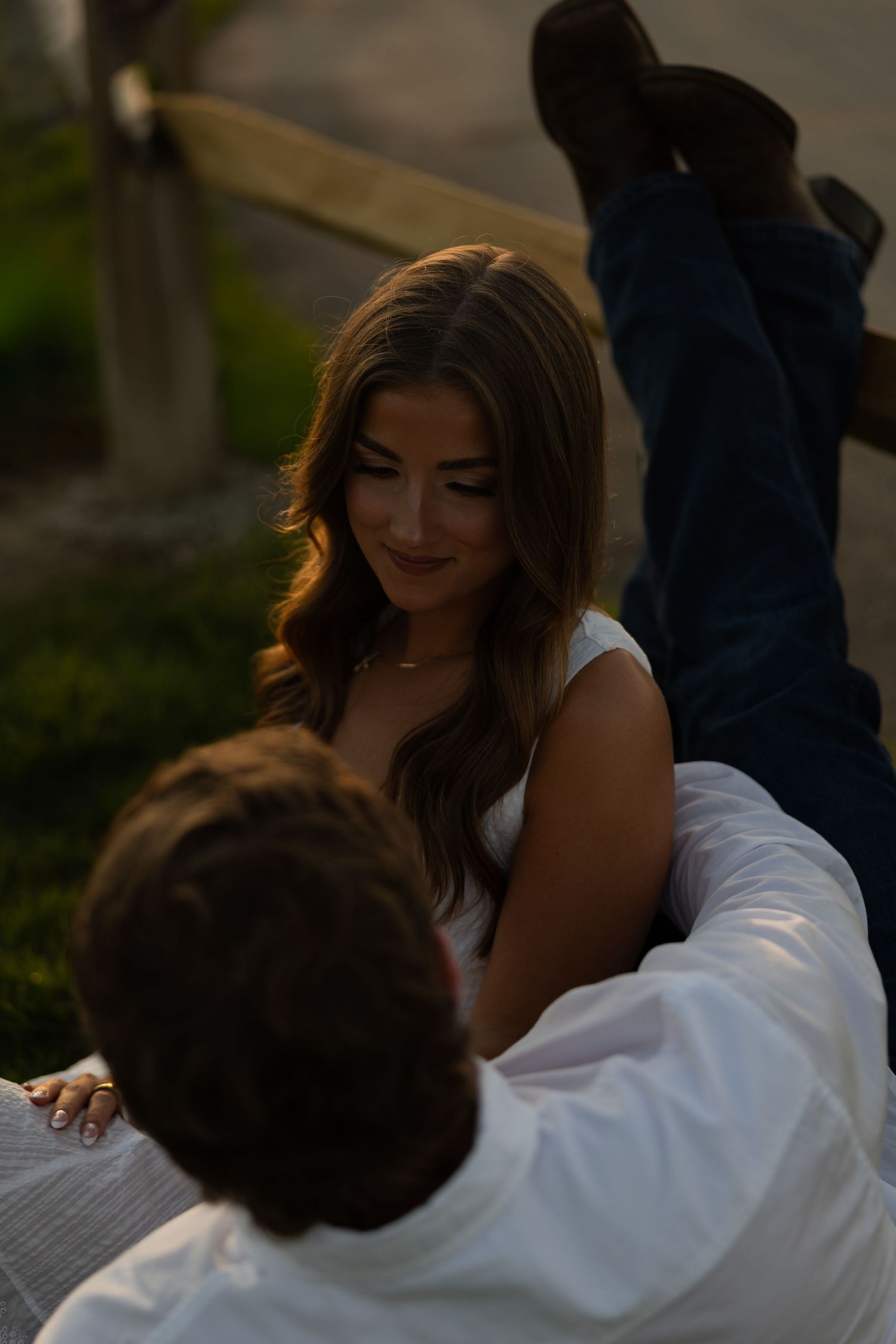 A woman in a white dress gazes softly at her partner during a romantic golden hour engagement session.