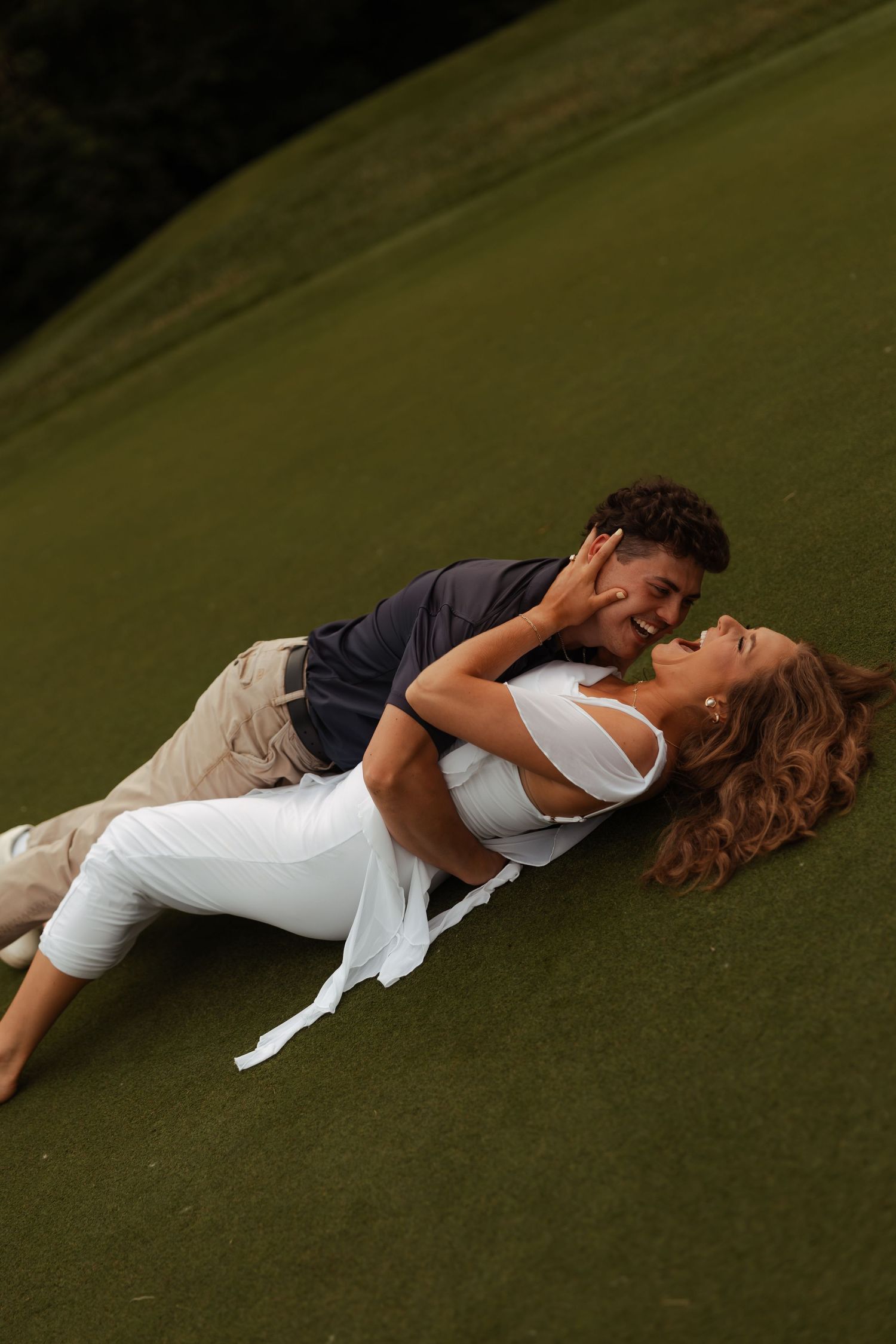 Romantic couple lying on a lush green golf course, sharing an intimate moment together.