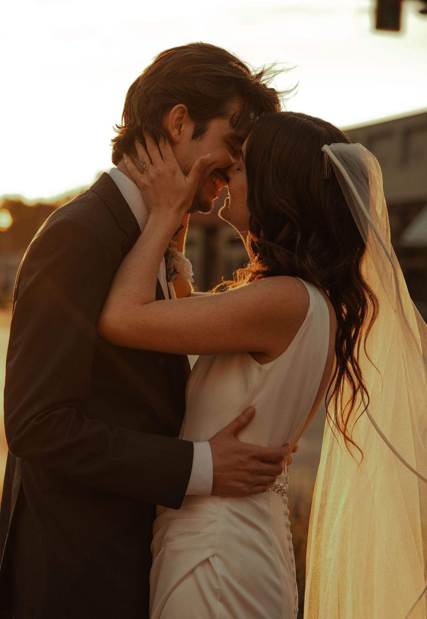 Bride and groom sharing a romantic golden hour kiss at their outdoor wedding ceremony.