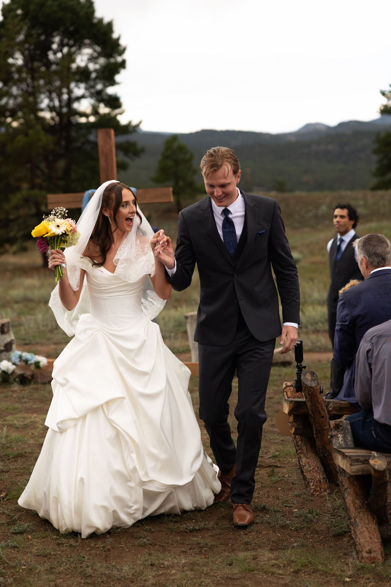 Bride and groom walk down outdoor aisle after wedding ceremony with mountain backdrop.