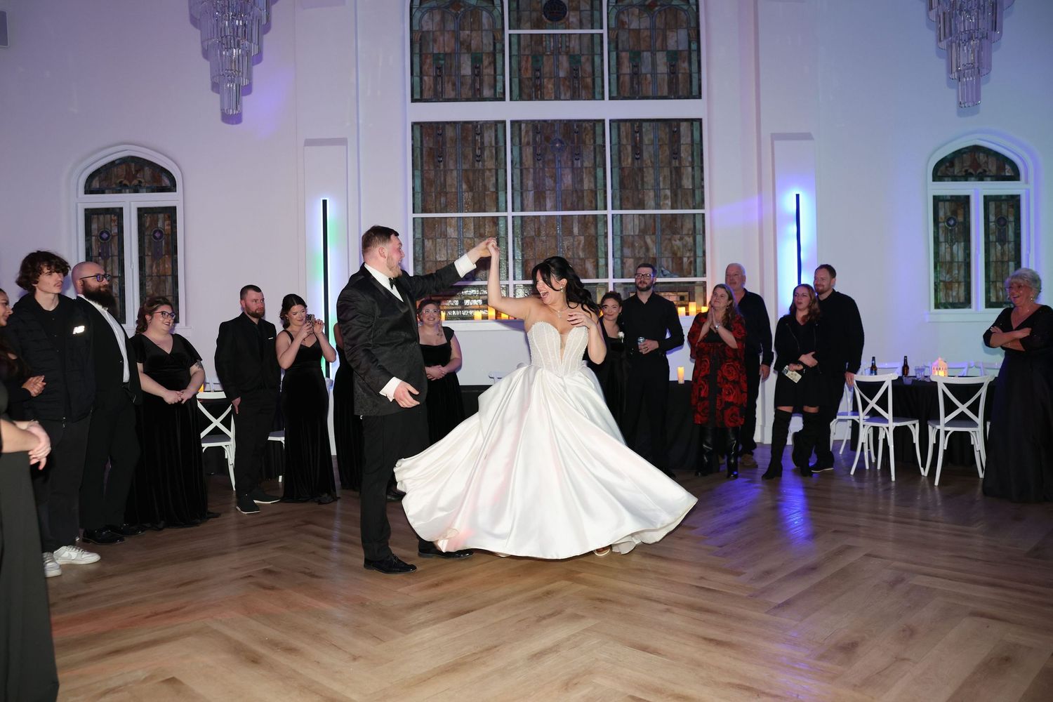 Bride and groom sharing elegant first dance in stunning ballroom with stained glass windows.