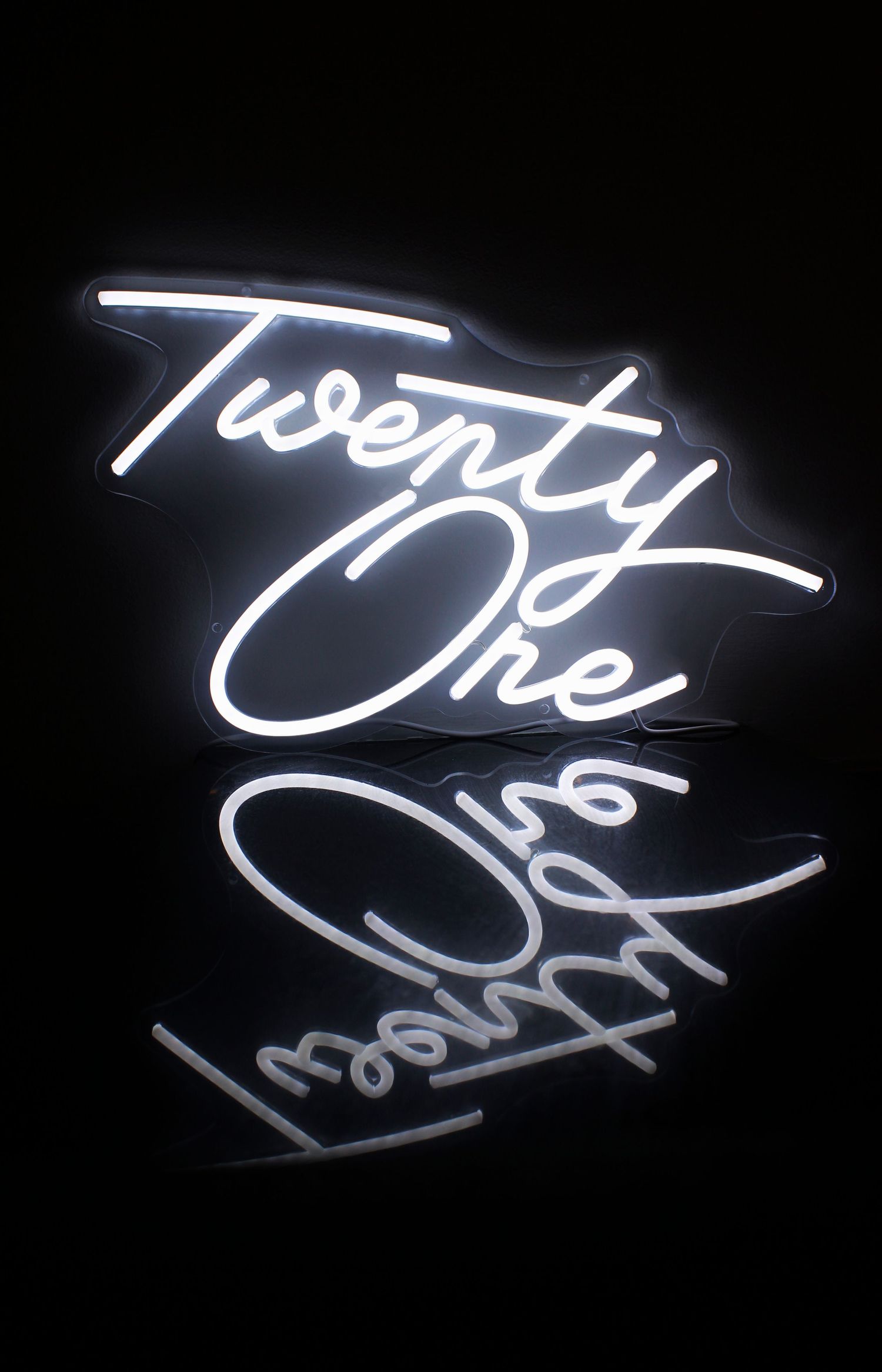 A glowing white neon sign reading Twenty One reflected on a shiny black surface in a dark room.