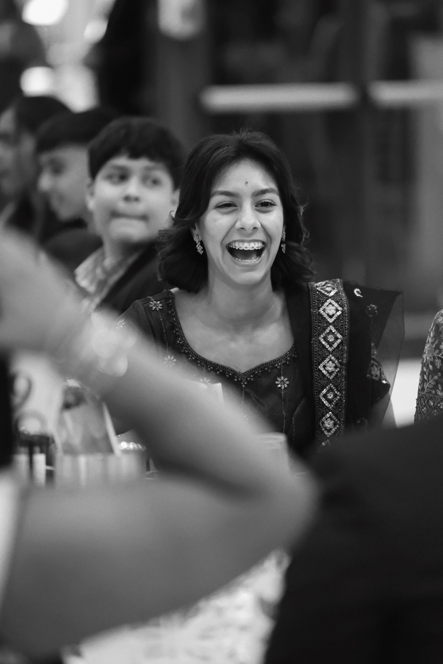 Black and white photo of a joyful woman laughing at a festive cultural celebration with others nearby.