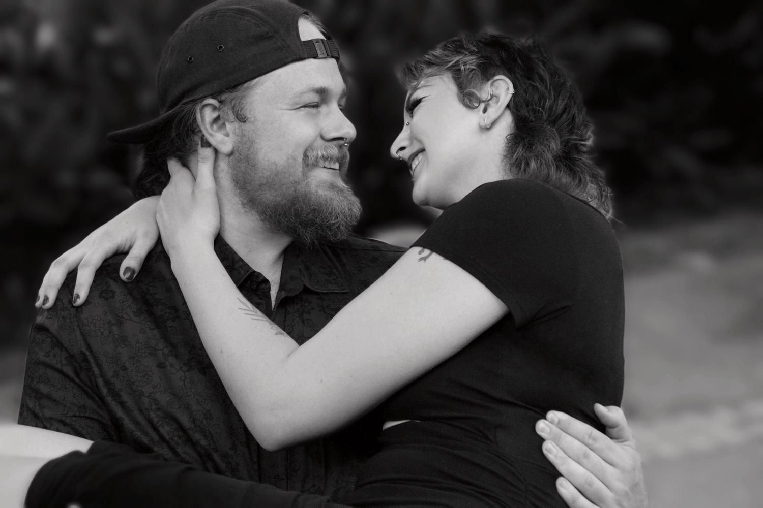 Black and white photo of smiling couple embracing outdoors in a tender romantic moment.