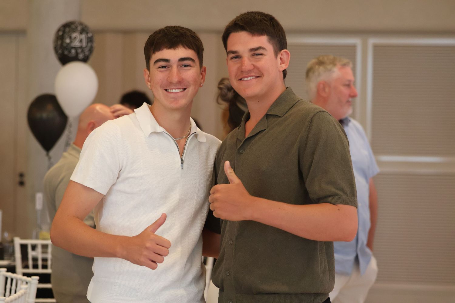 Two young men smiling and giving thumbs up at a black and white themed celebration event.