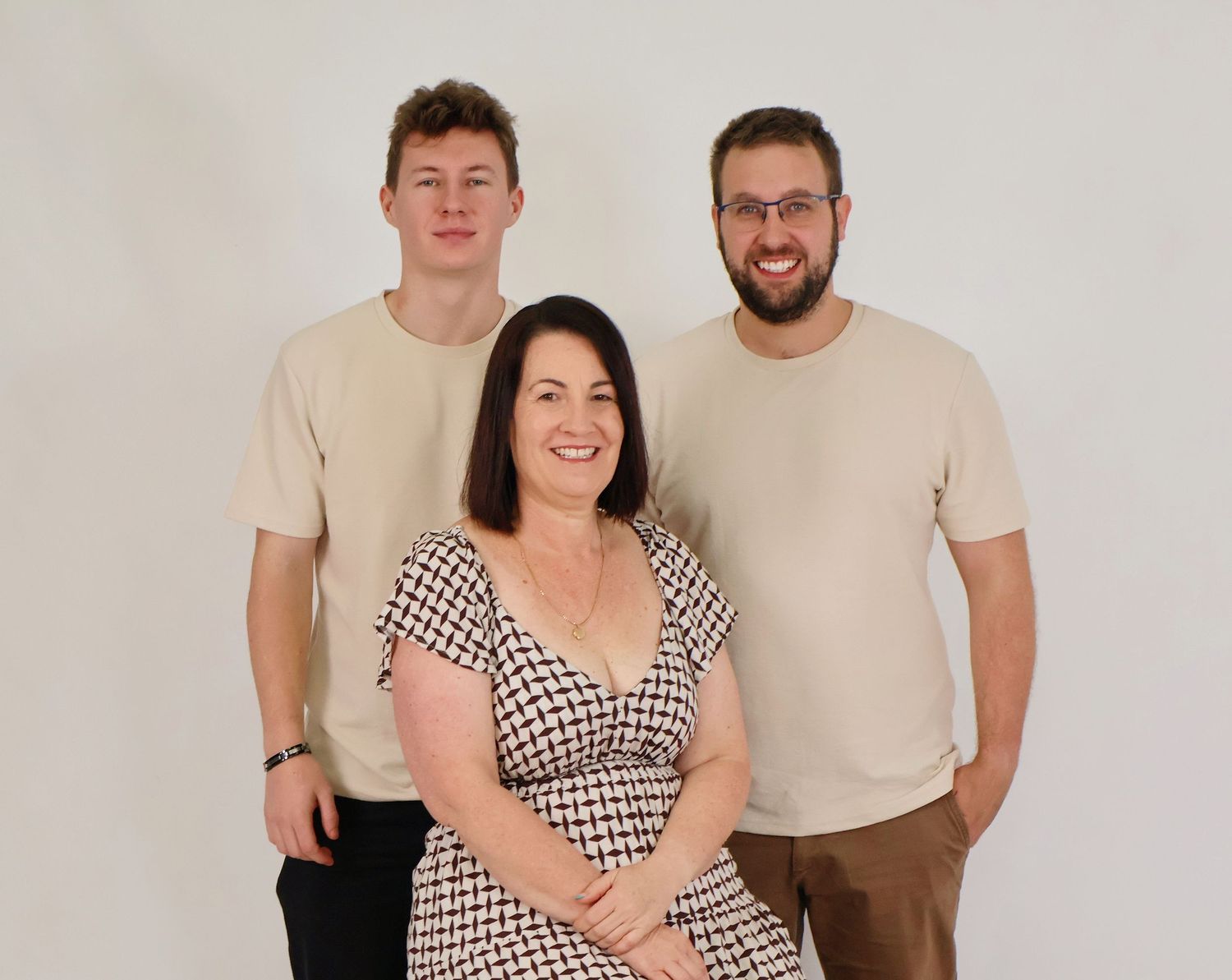 Professional family portrait of a mother seated between her two adult sons against white backdrop.