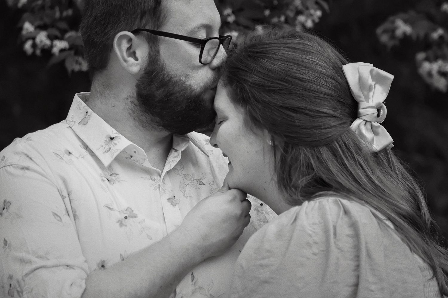 Black and white close-up of couple sharing an intimate moment, man kissing womans forehead outdoors.