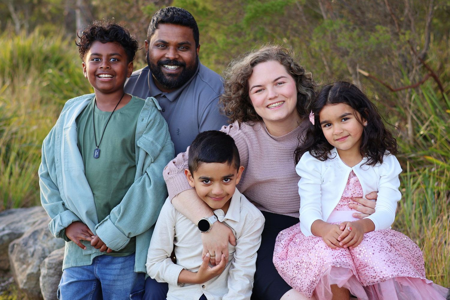 Happy interracial family of five with three children posing outdoors in nature.